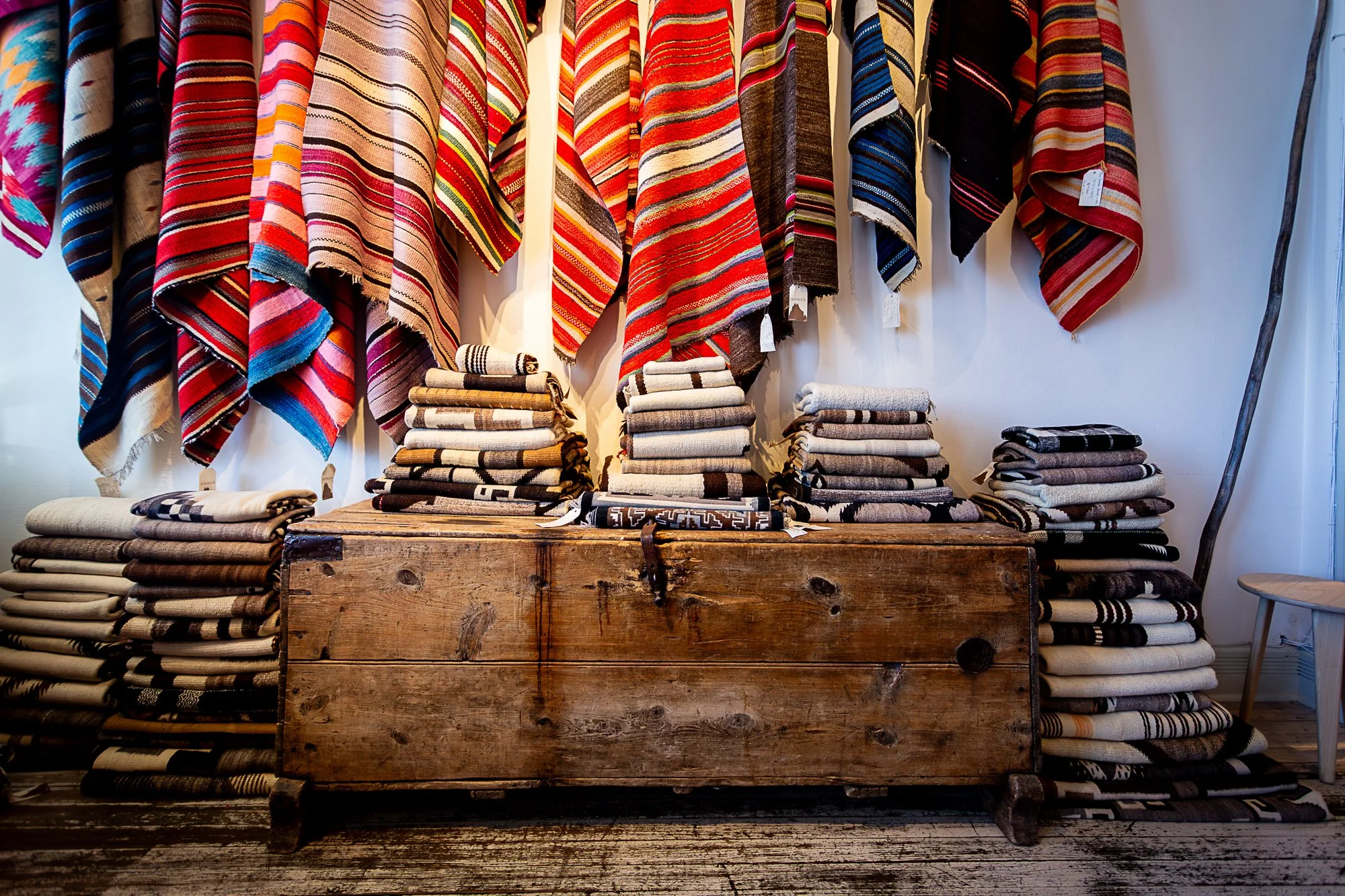 Display of colorful native american striped textiles and folded blankets or rugs on wooden trunk in Shiprock Santa Fe, a shop in New Mexico.