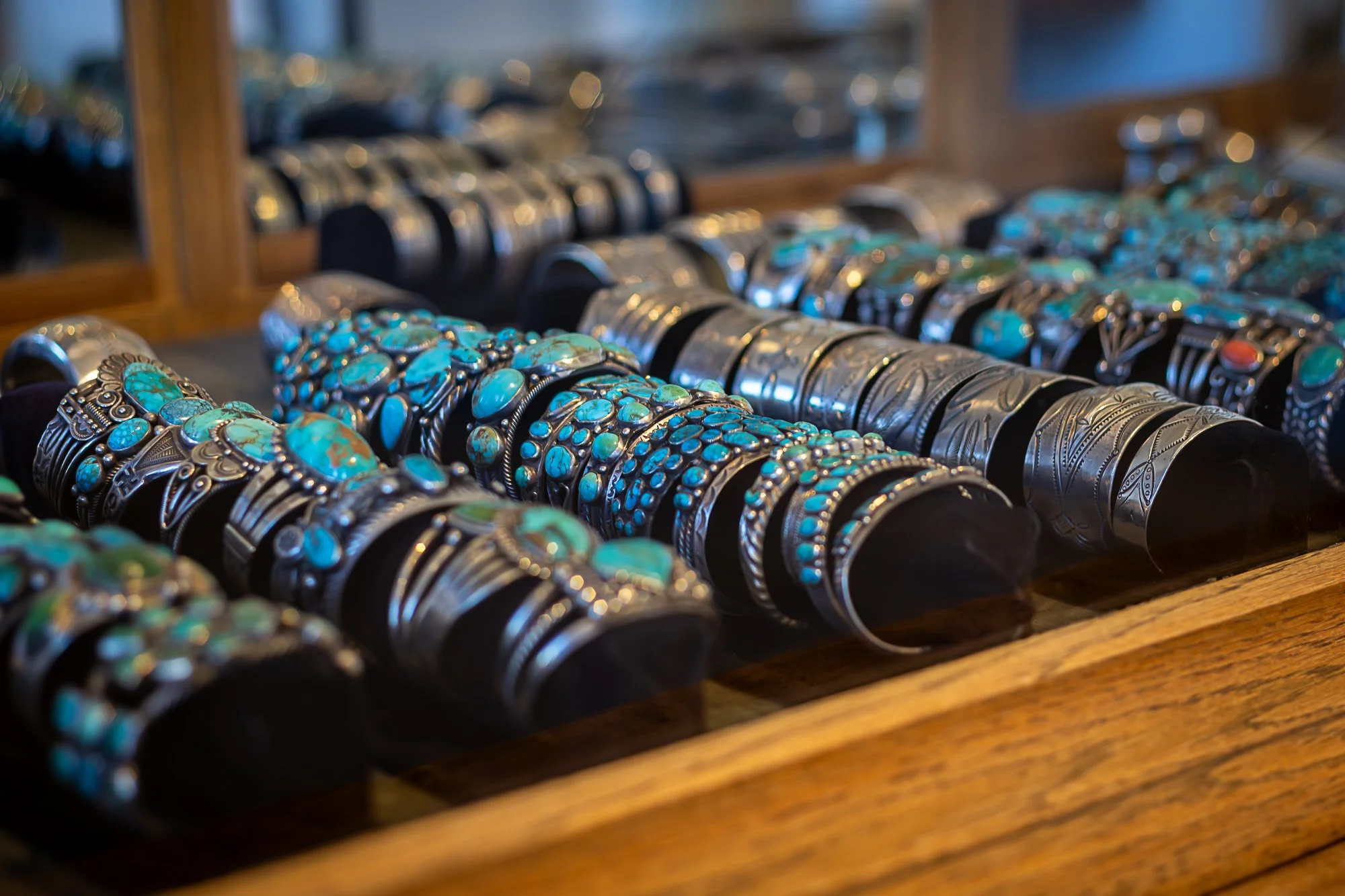 Display of various silver and turquoise jewelry bracelets on a wooden table.