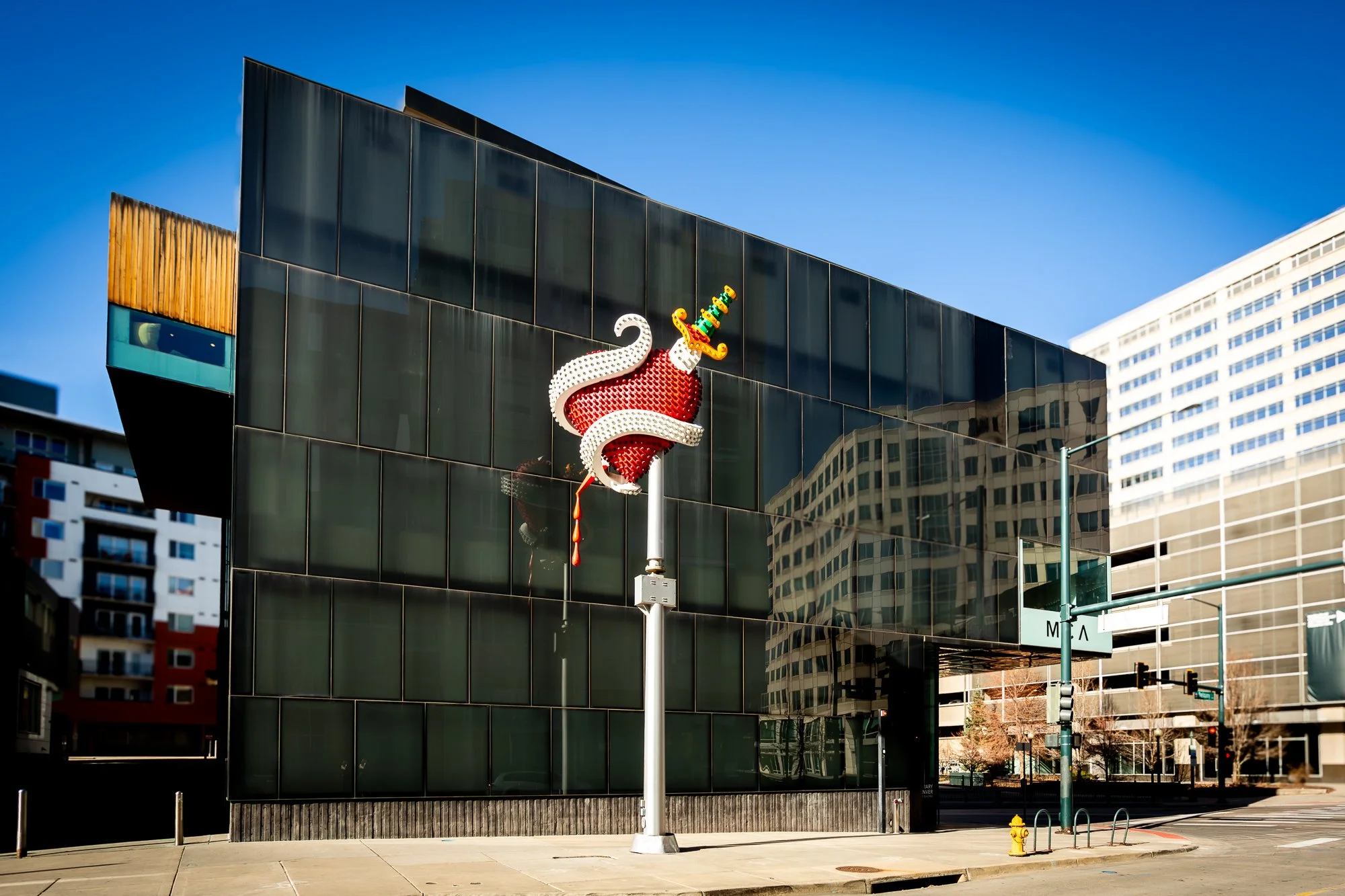 Modern city building with a reflective glass facade and a large lightning bolt sculpture of a stylized chili pepper with a face, hat, and tongue.