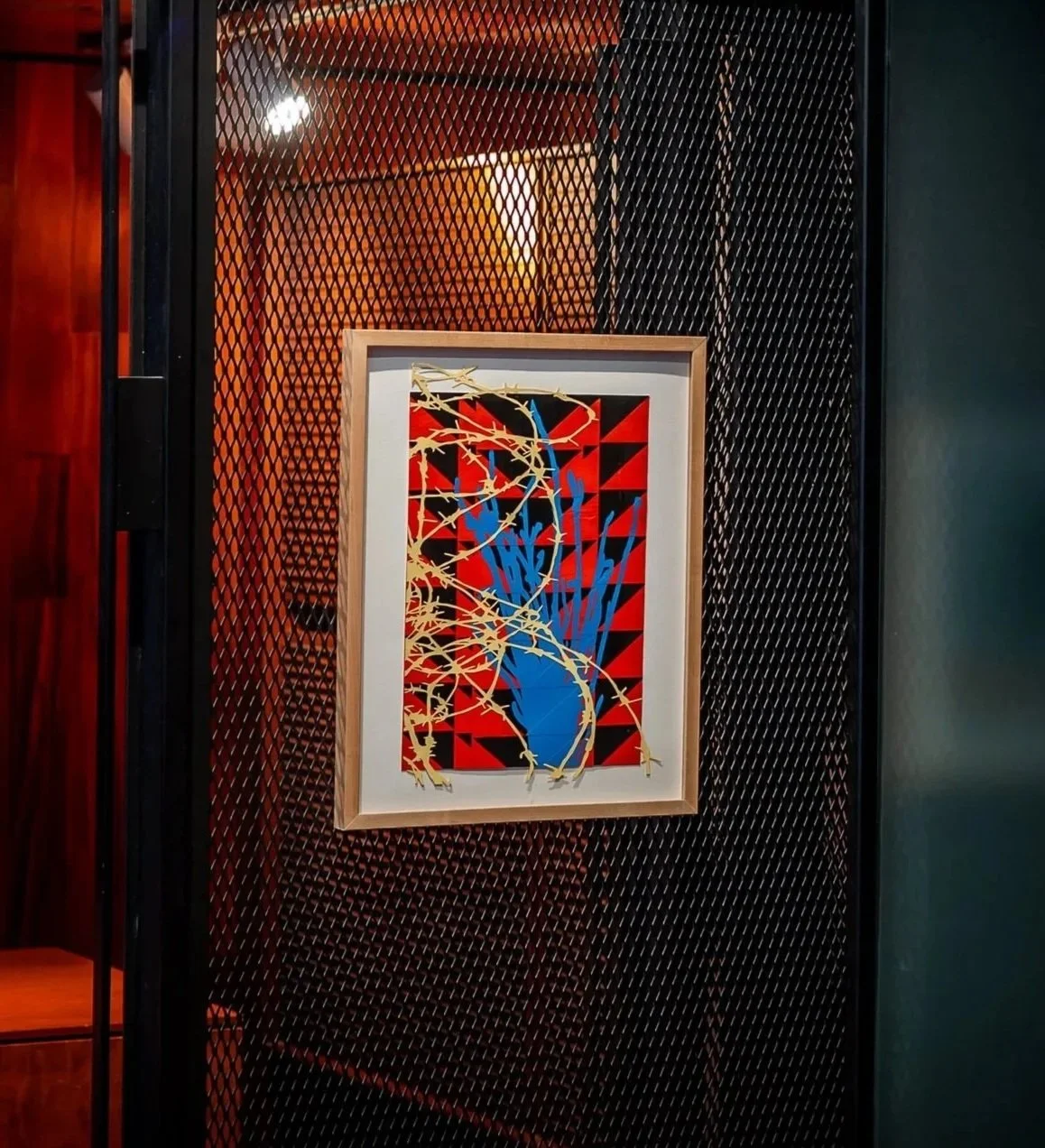 Artwork featuring gold branches over blue vase on red and black geometric background.