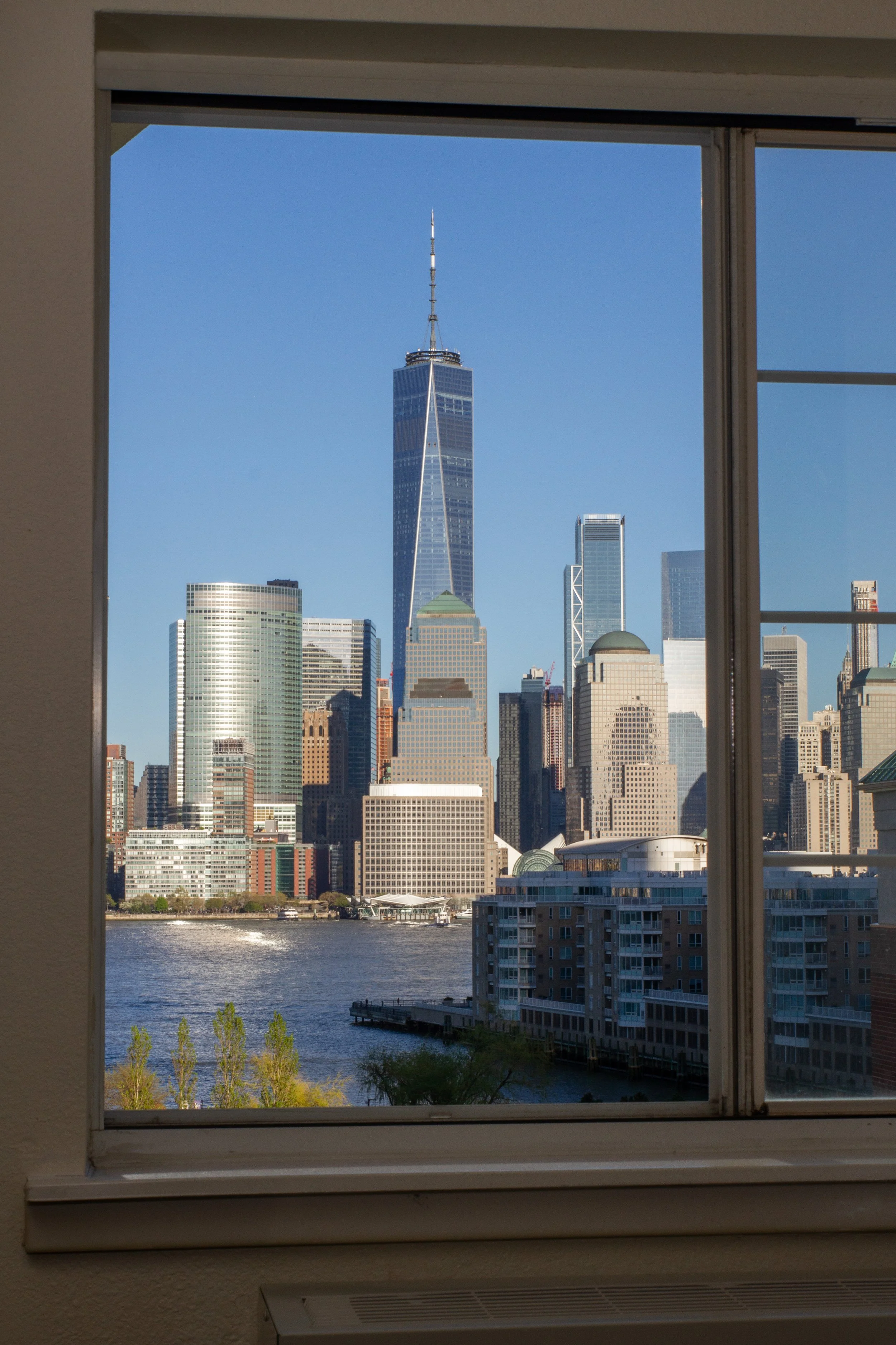 View of Manhattan skyline through a window, including One World Trade Center, in New York City.