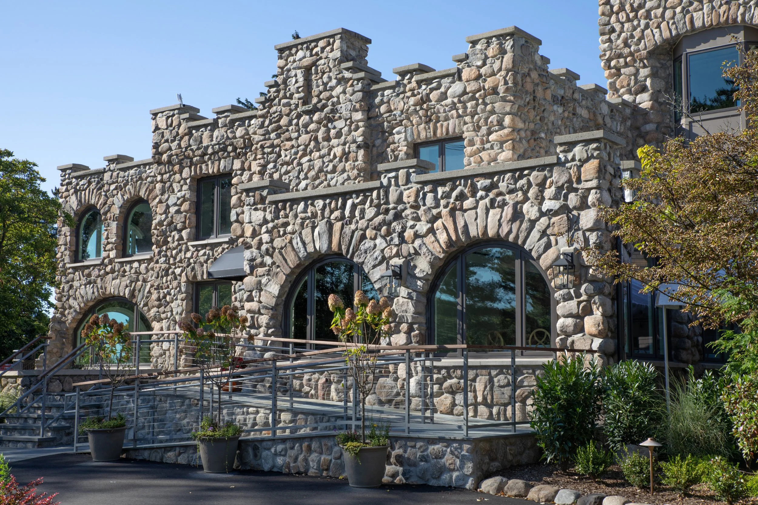 Building made of large, rounded stones with arched windows, a stone terrace, and potted plants outside.