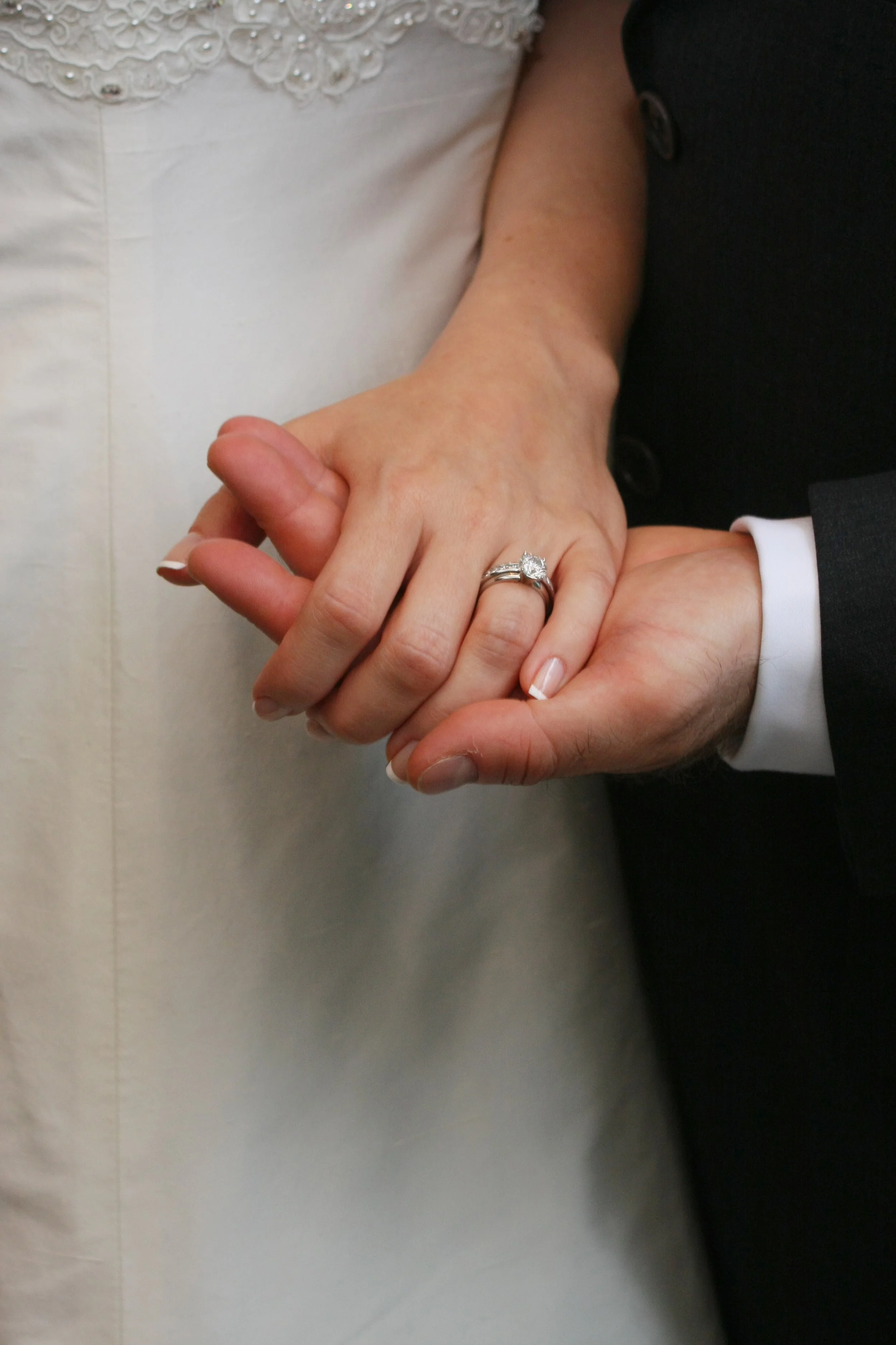Close-up of a bride and groom holding hands, showing a wedding ring on the bride's finger.
