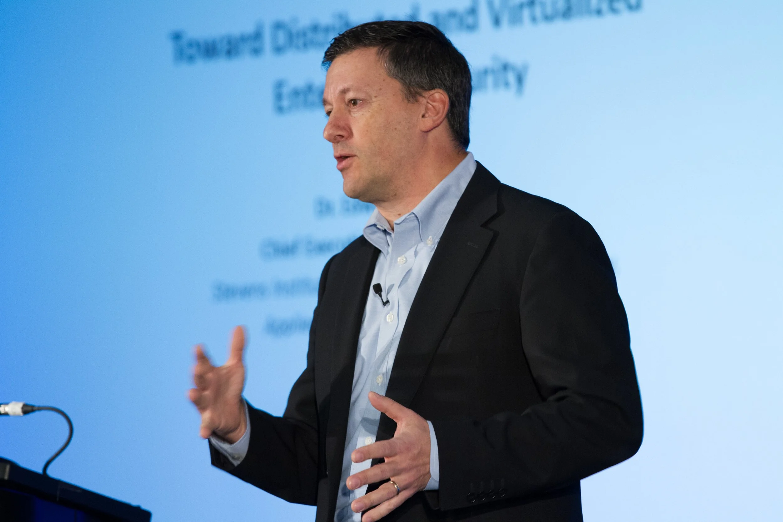 A man in a suit giving a presentation in front of a slide with partially visible text.