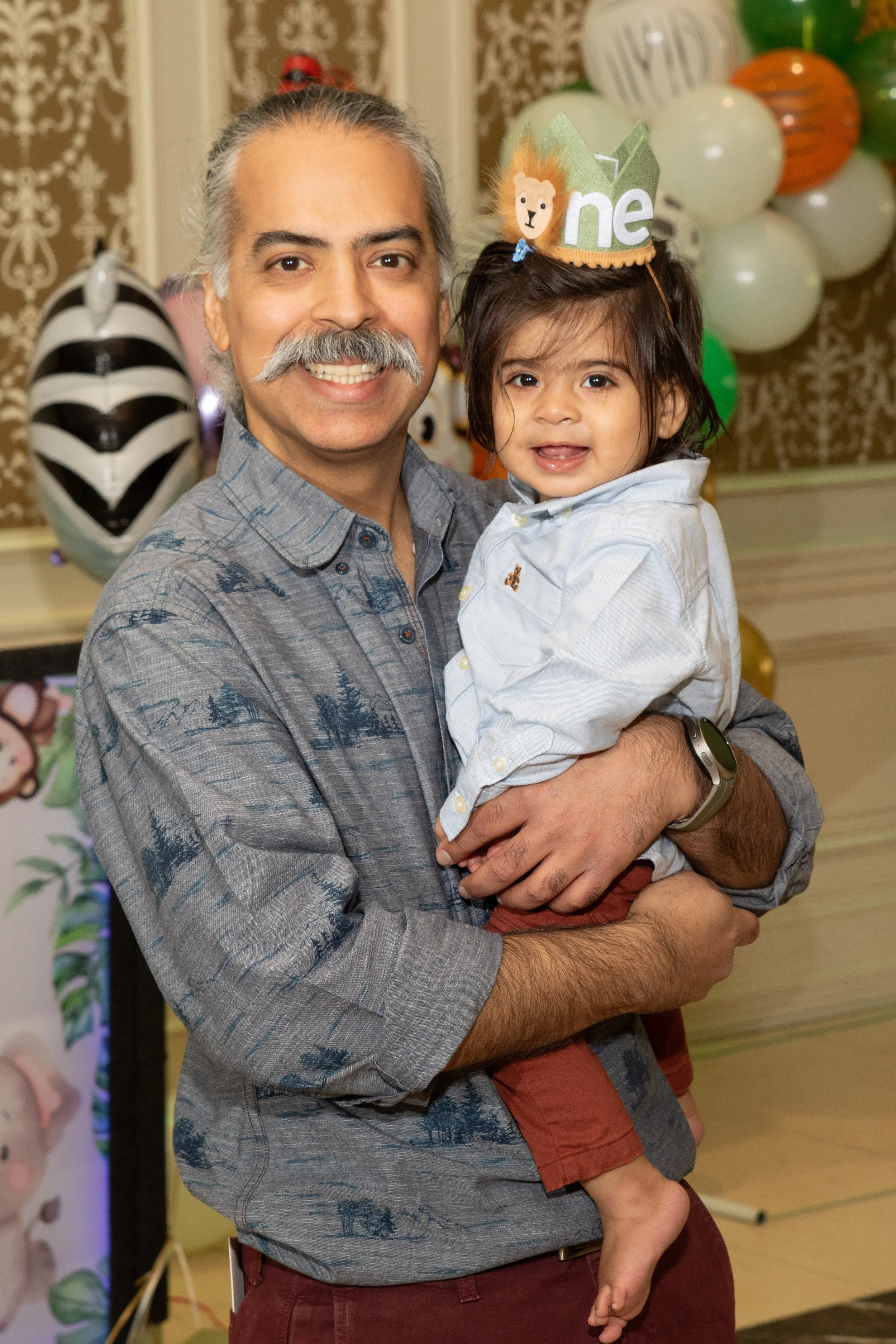 A man holding a young girl at a birthday celebration at the Terrace in Paramus NJ, with balloons and party decorations in the background.