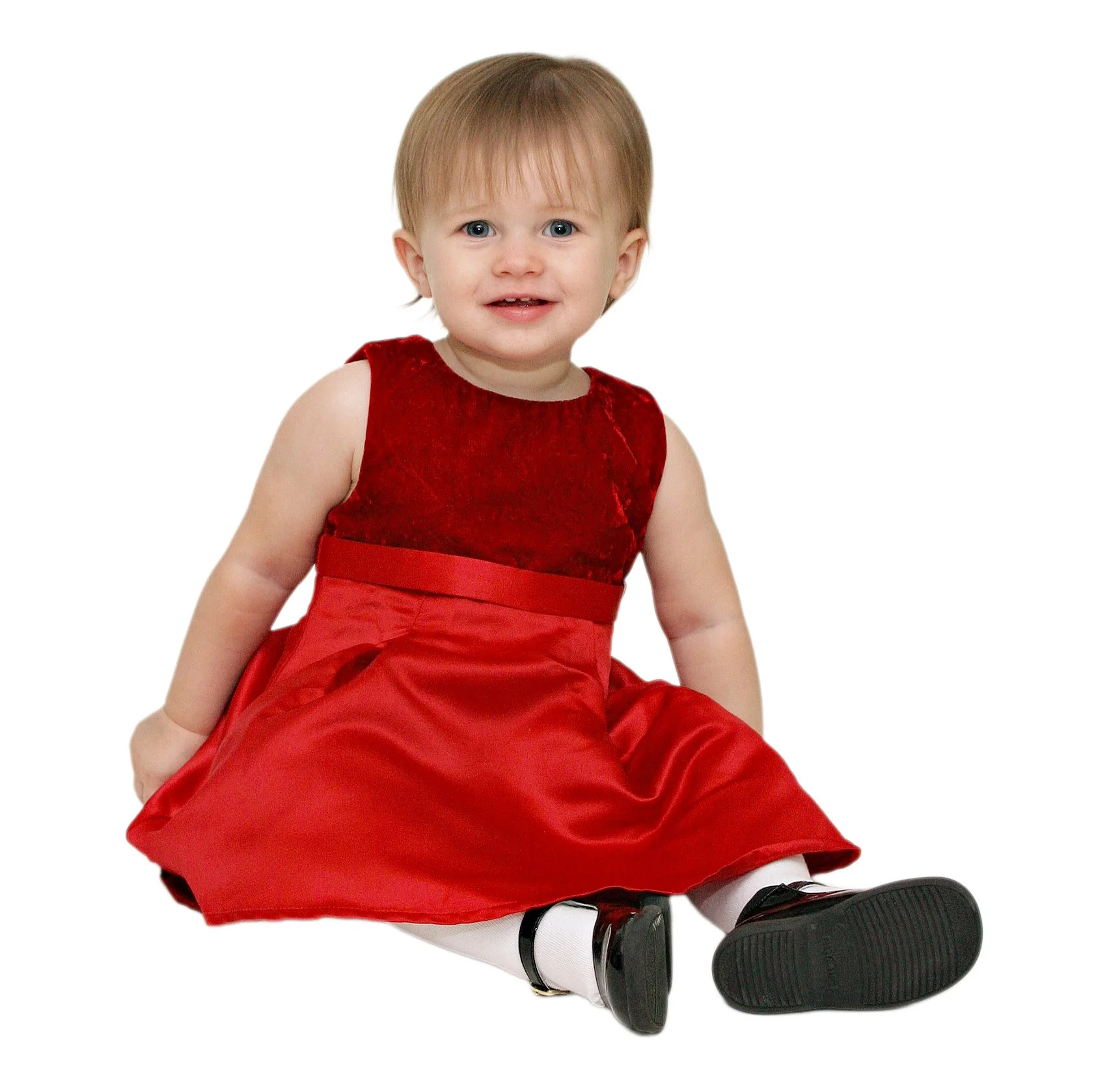A young girl portrait wearing a red dress, white tights, and black shoes, sitting on the floor and smiling.