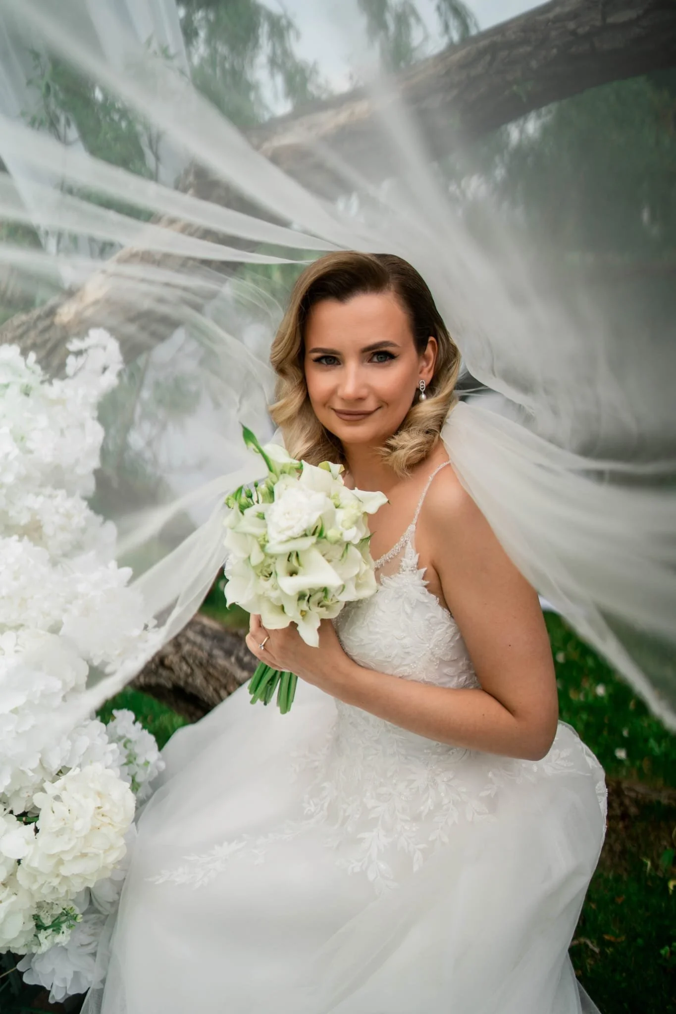 A bride with blonde hair photographed beneath her veil in a white dress holding her white bridal boquet