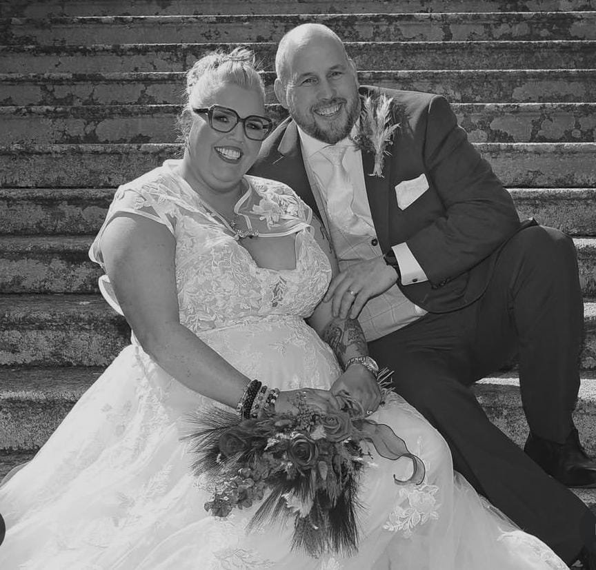 A black and white of a bride in her white dress and new husband sitting on steps in the haven hotel dunmore east
