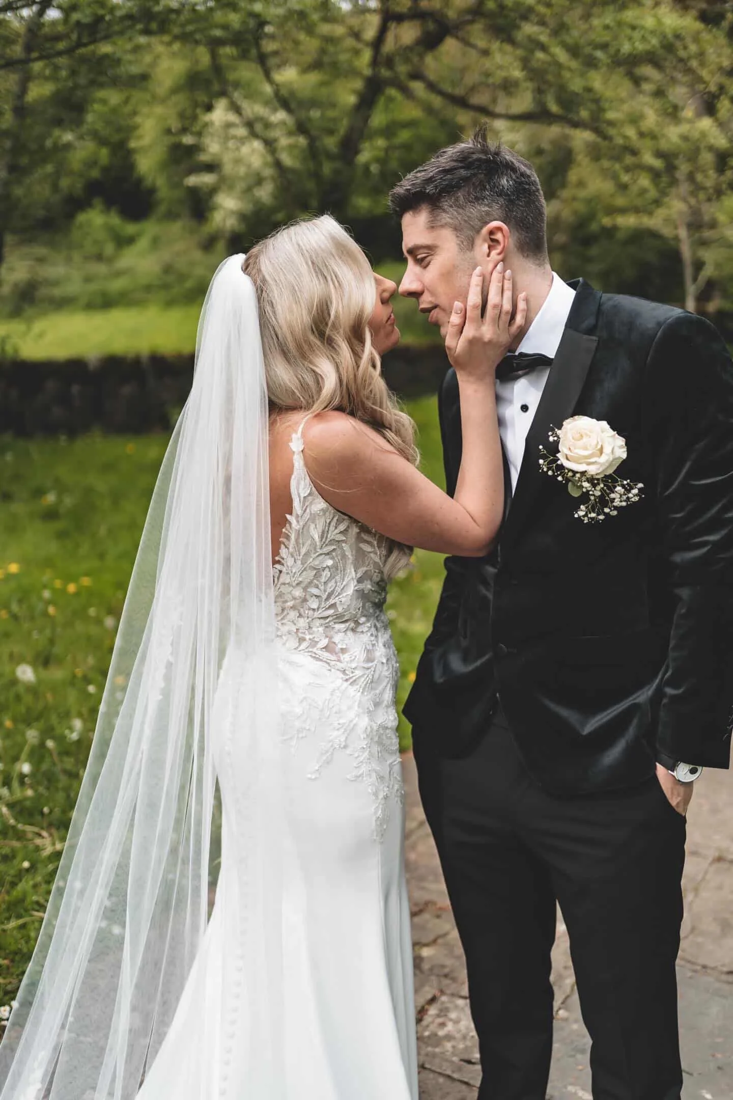 Bride and groom kissing in St Patricks Well Clonmel, Co. Tipperary. Groom is wearing a tuxedo and the bride is wearing a lace detailed low back fitted dress.