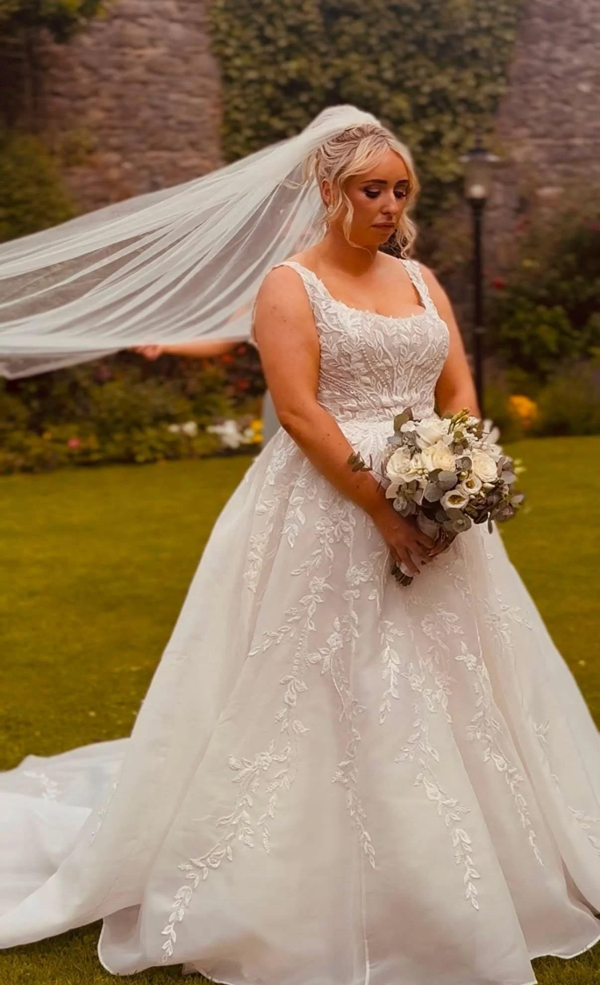 A bride wearing her lace square neck  bridal dress holding her white bouquet and floating veil at hotel kilkenny 