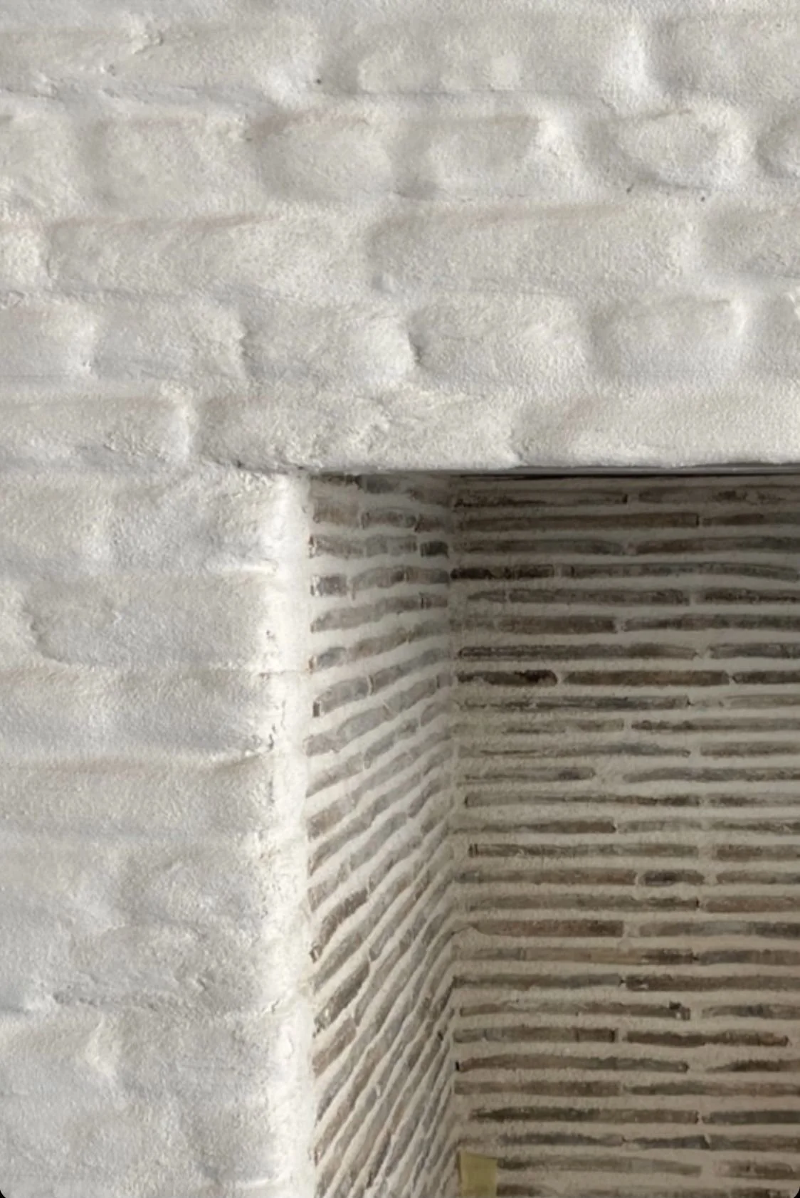Close-up of a corner of a wall with textured white cement finish and striped pattern on an adjacent wall.