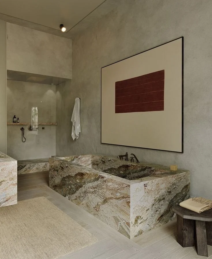 Modern bathroom with a marble soaking tub, a walk-in shower with a built-in shelf, wall-mounted faucet, and a large abstract artwork on the wall.
