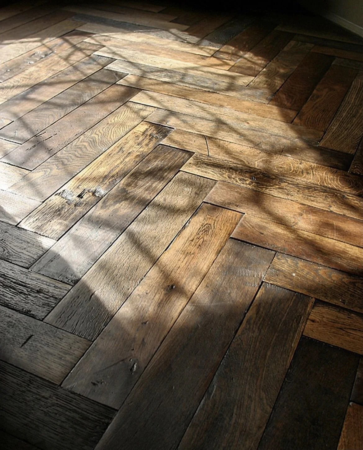 Close-up of a wooden herringbone patterned floor with sunlight and shadows.