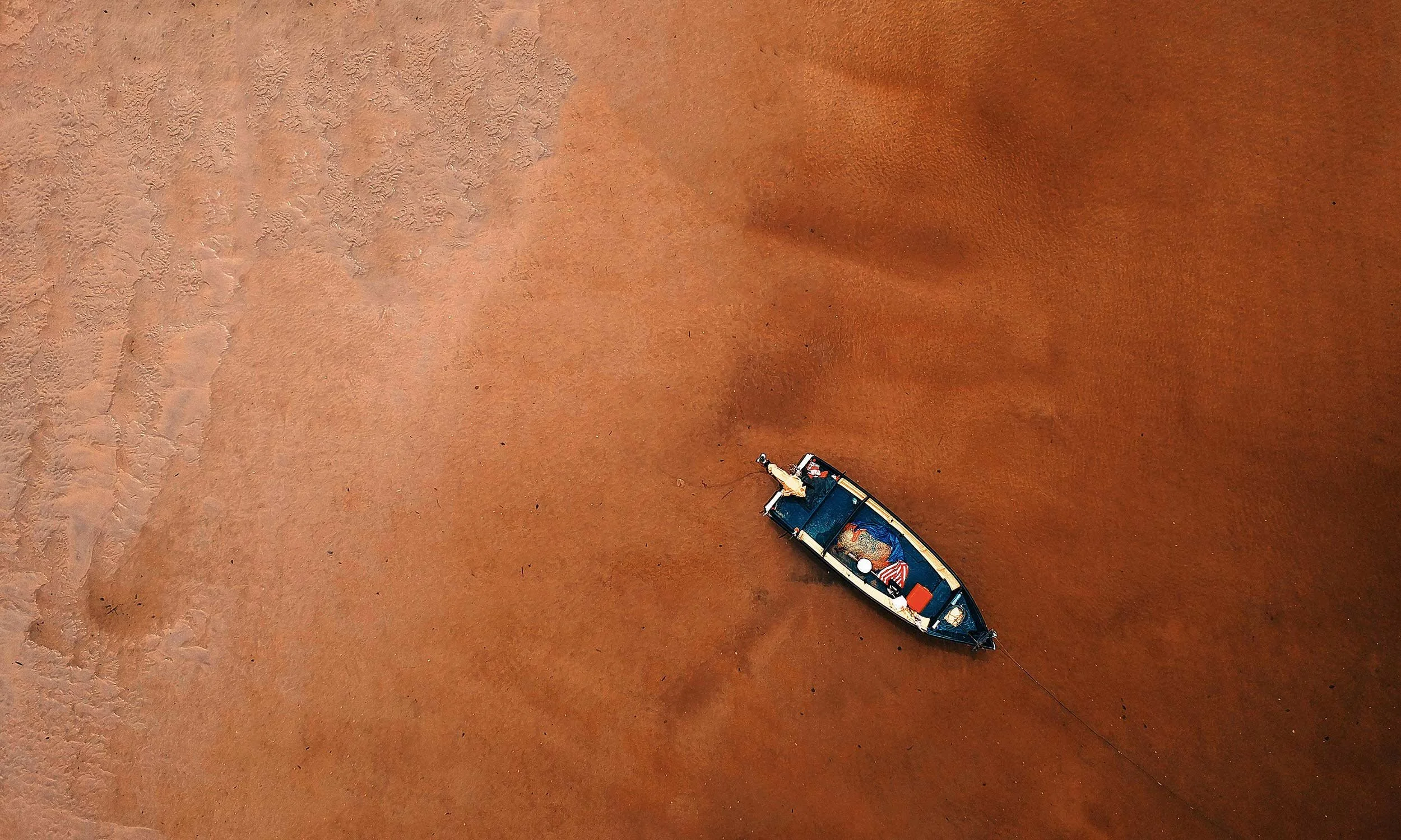 A boat on a muddy, reddish-brown shoreline, viewed from above