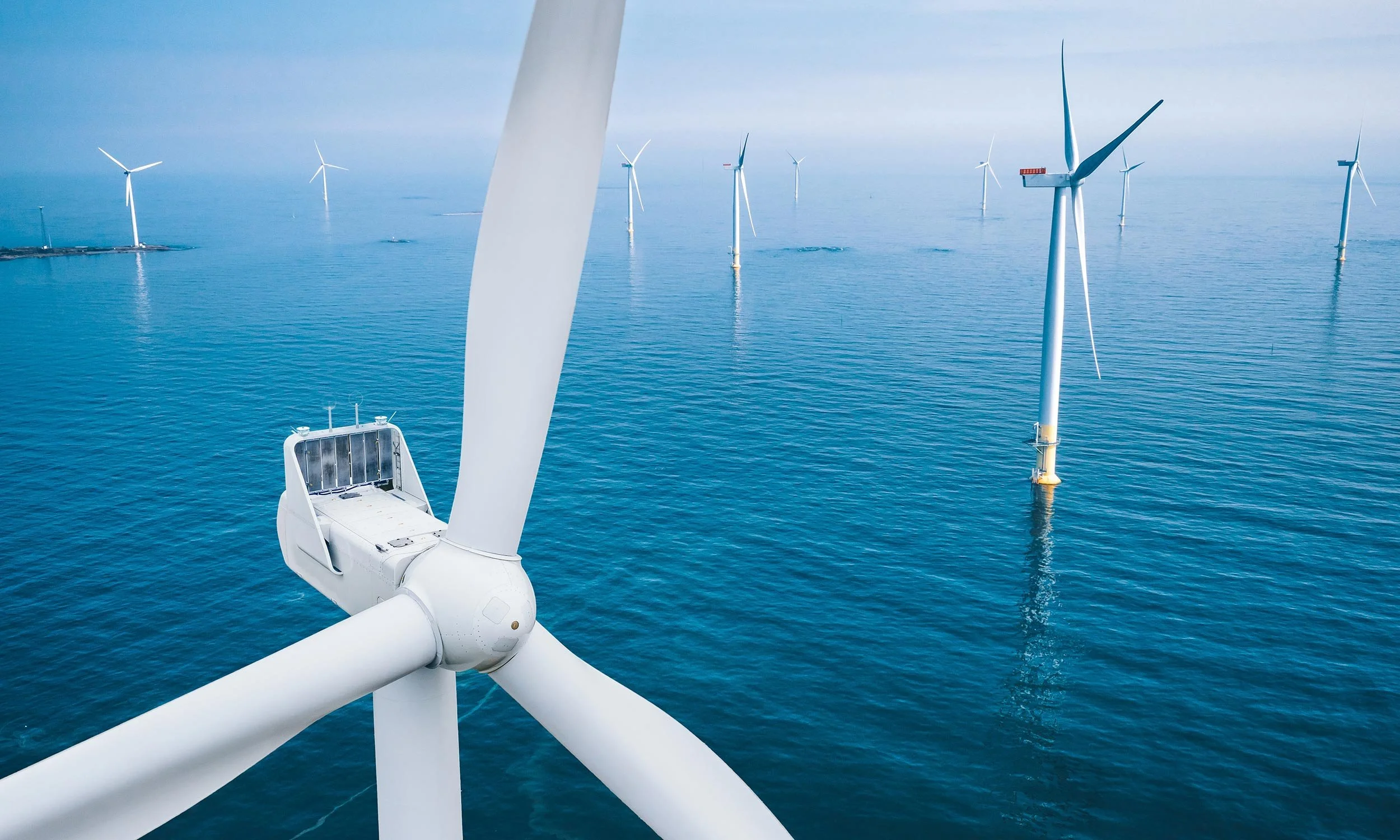 Offshore wind turbines in the ocean, with one turbine prominently in the foreground and several others in the distance.