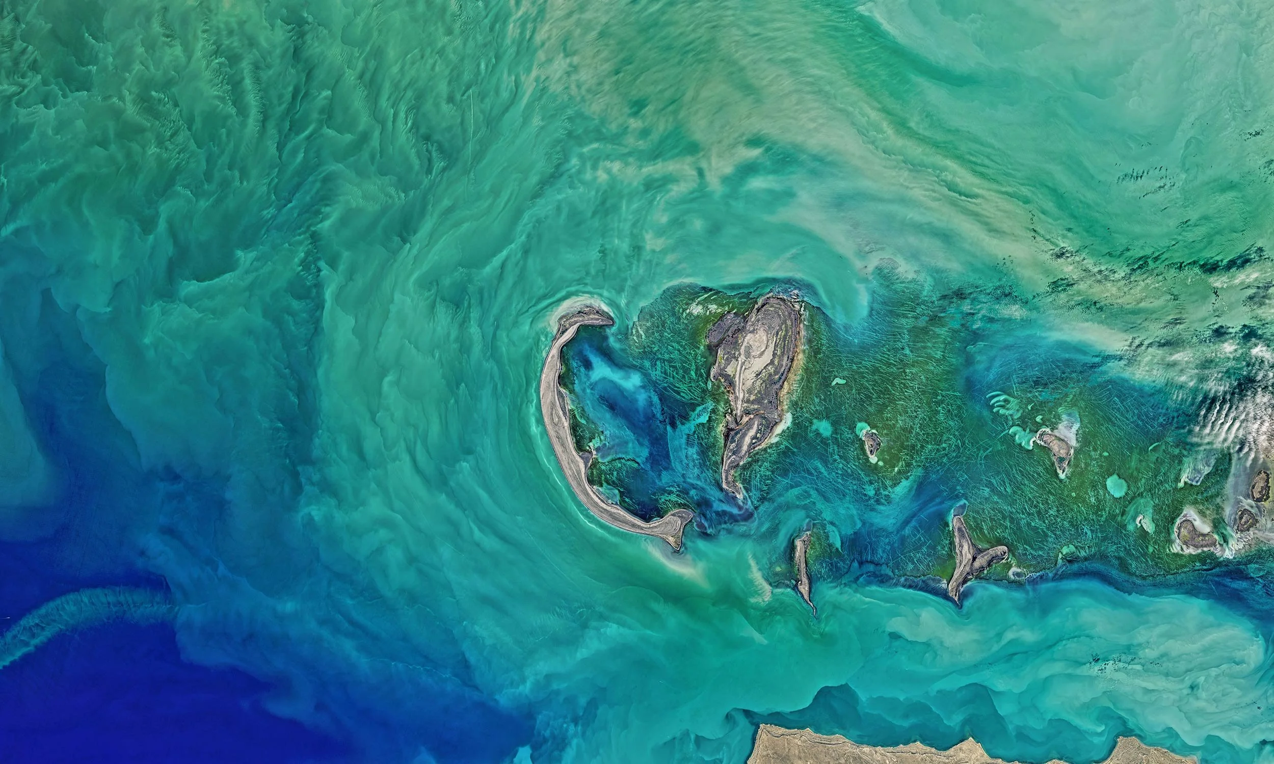 Satellite image of an island with surrounding turquoise and deep blue waters, showing land formations and coral reefs.