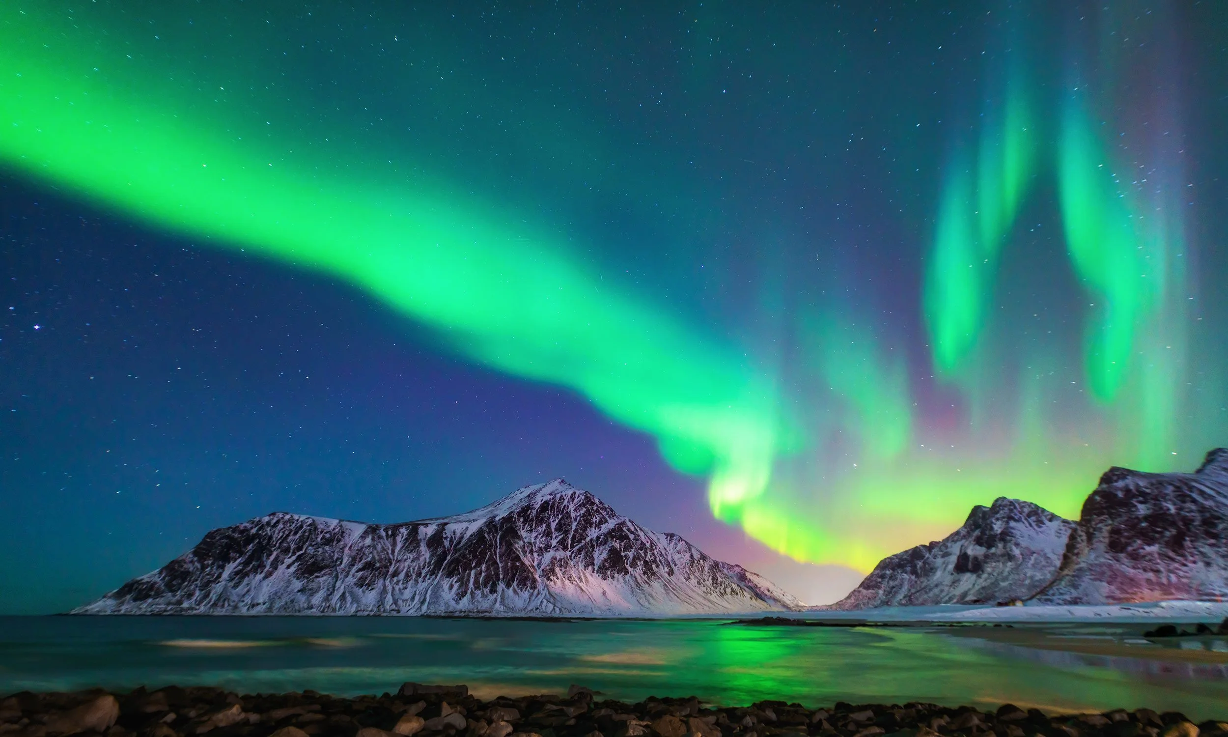 Northern lights over snow-capped mountains and ocean, night sky with stars.