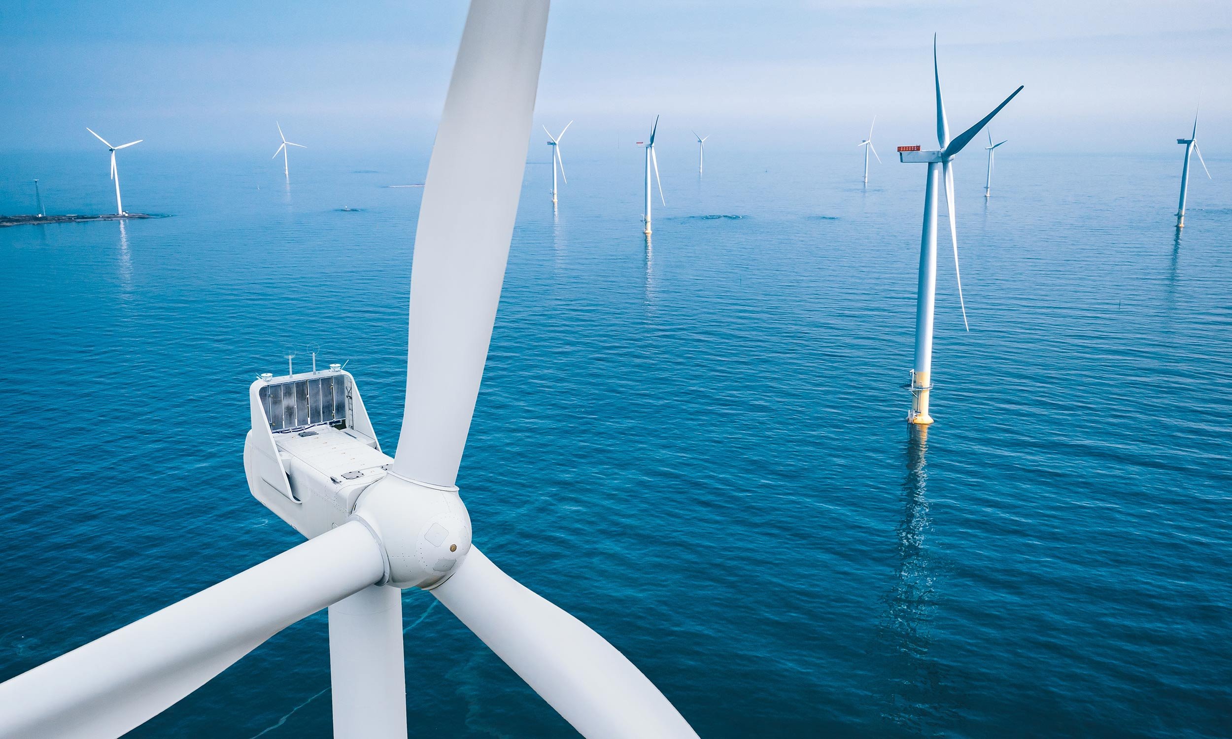 Offshore wind turbines in the ocean, with blue sky and calm water