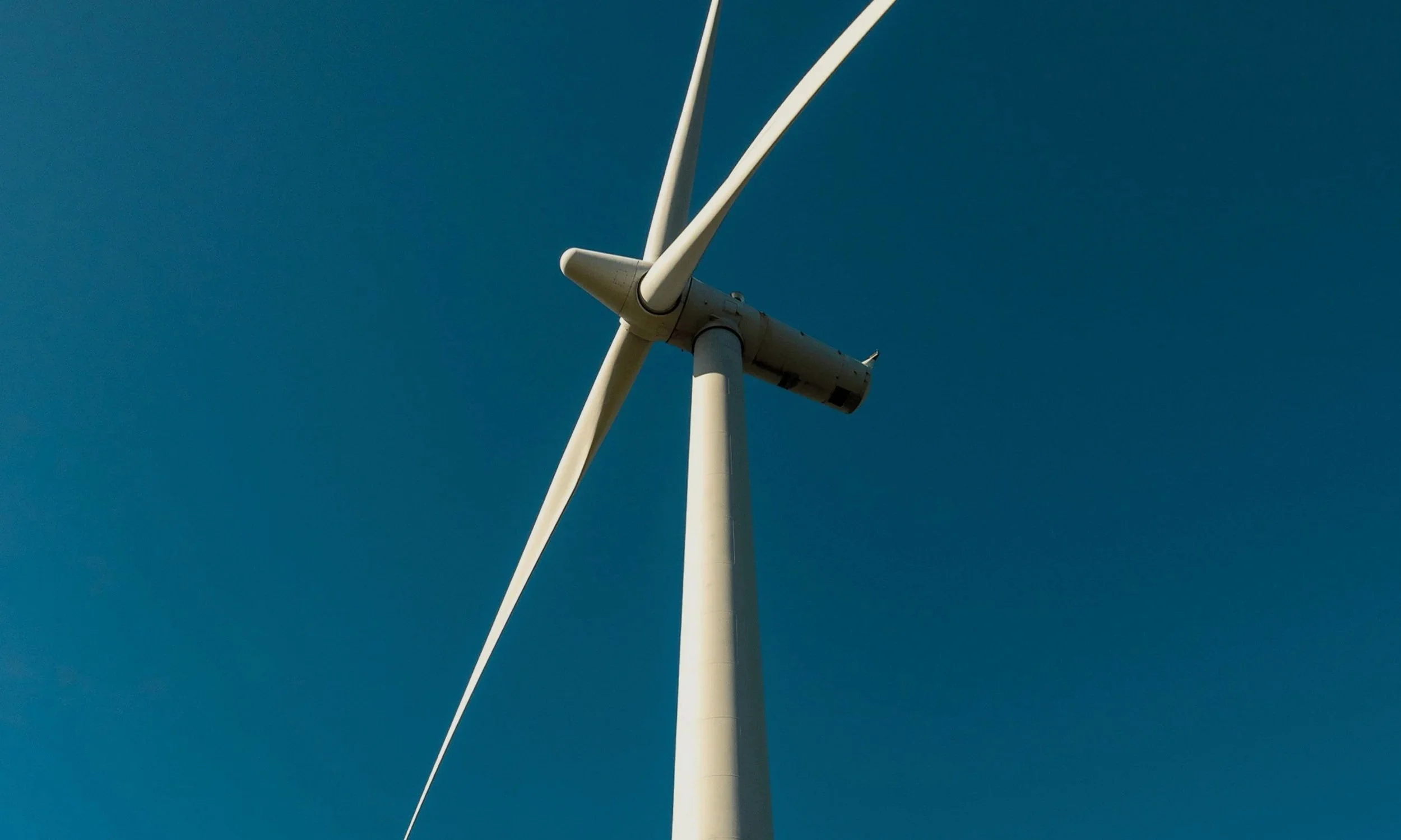 A white wind turbine against a clear blue sky.