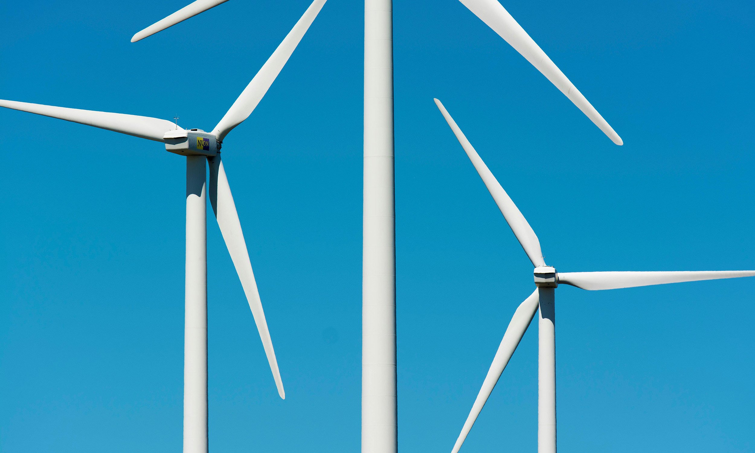 Three white wind turbines against a bright blue sky.