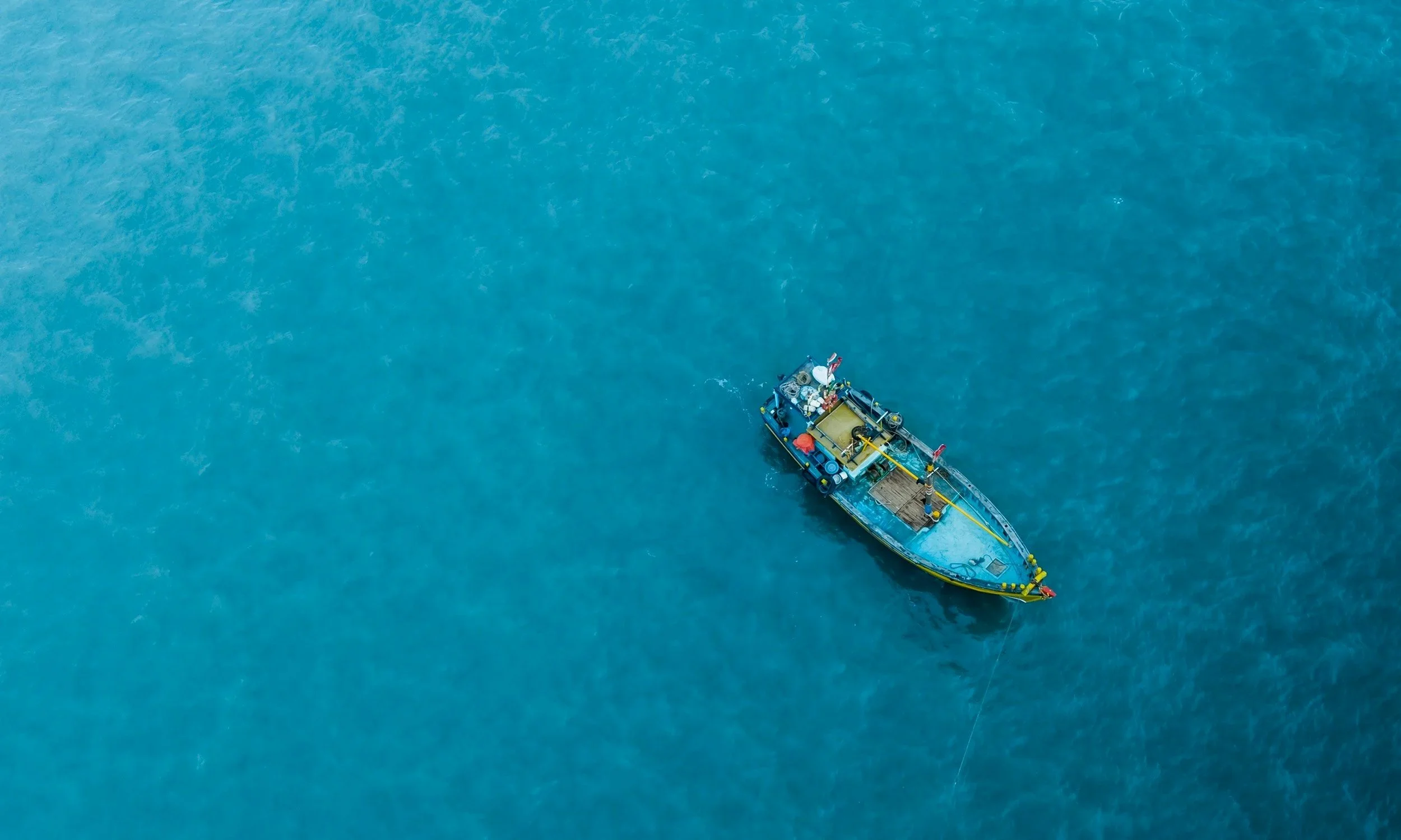 A yellow boat floating in the blue ocean, viewed from above.