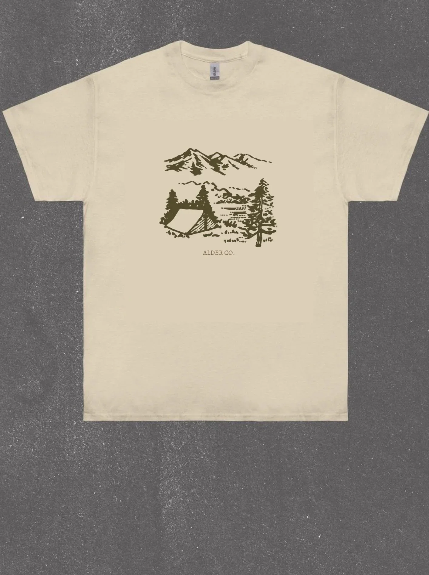 Cream-colored T-shirt with a black line drawing of a mountain range, trees, and a tent. The text 'ALDER CO.' is printed below the illustration.