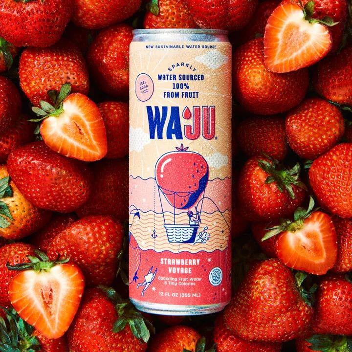 A can of Waju Strawberry Voyage sparkling fruit water surrounded by fresh strawberries, some halved to show the inside.