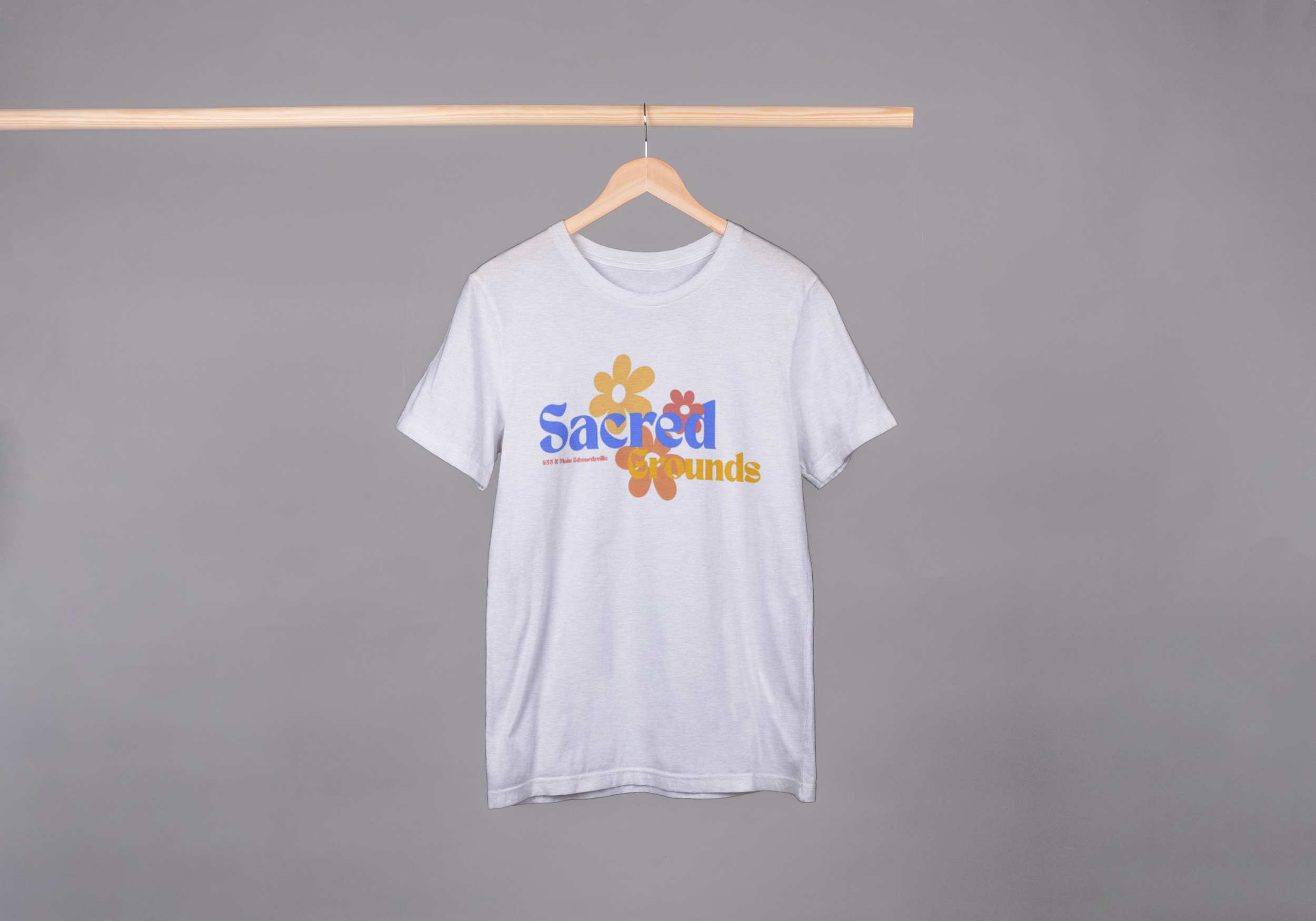White T-shirt with colorful text and flowers hanging on a wooden hanger against a gray background.