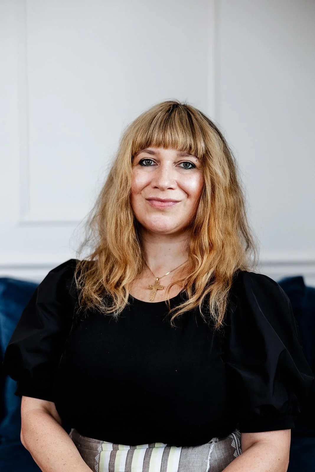 A woman with long blonde hair smiling, with a light background.