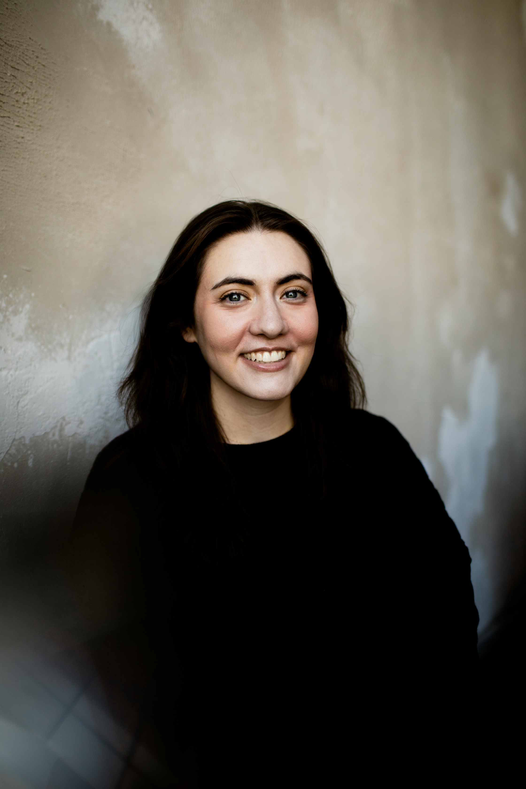 A woman with long brown hair smiling, with a light background.