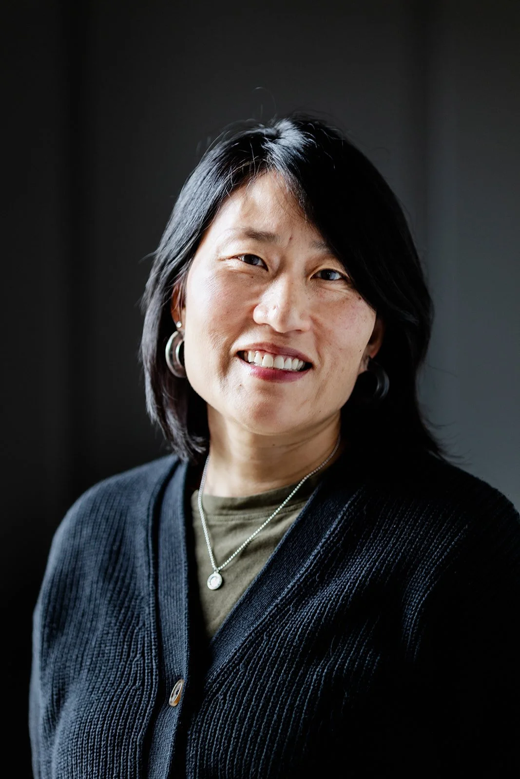 Close-up photograph of a woman with shoulder-length dark hair wearing a sweater looking at the camera.