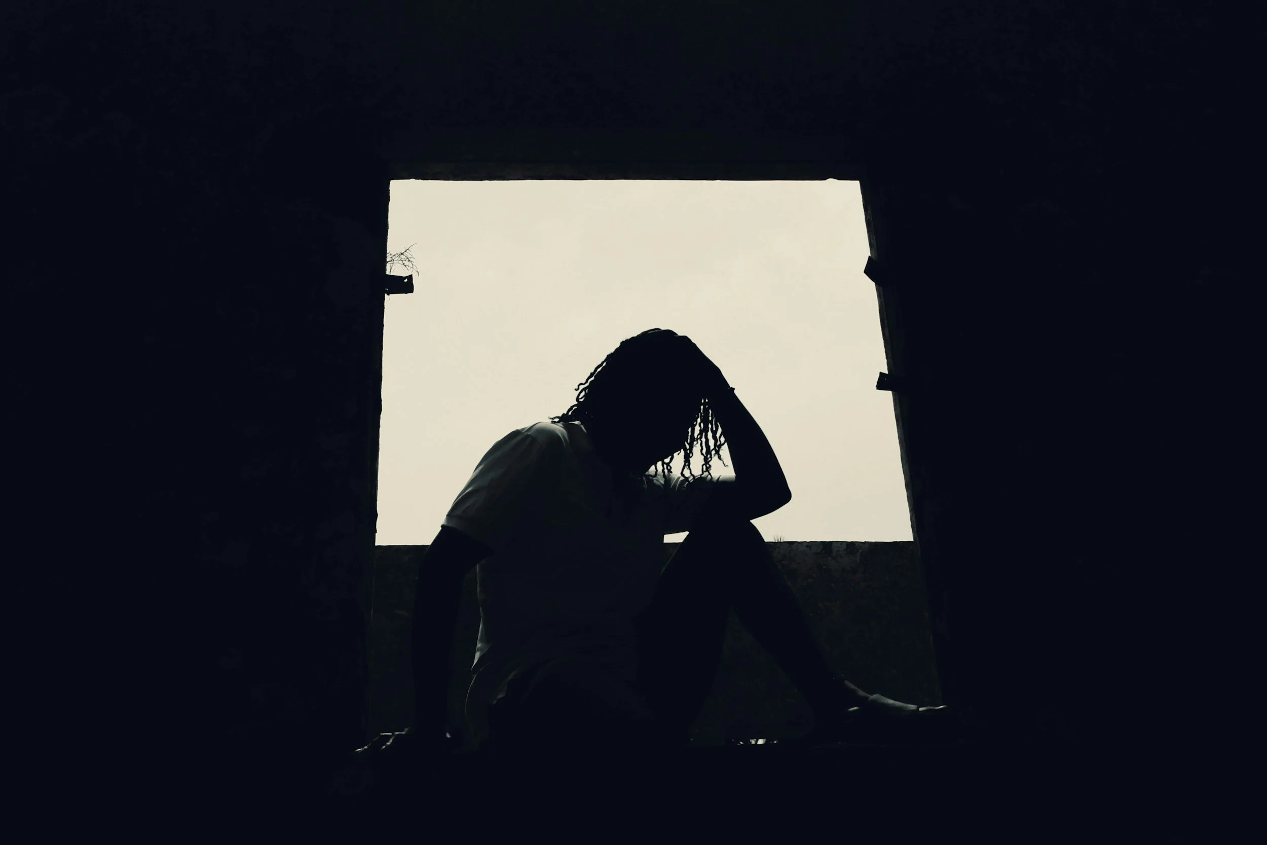 Silhouette of a woman sitting alone with her head in her hand, framed by a dark doorway. PMDD and relationships, women's therapy Woking.