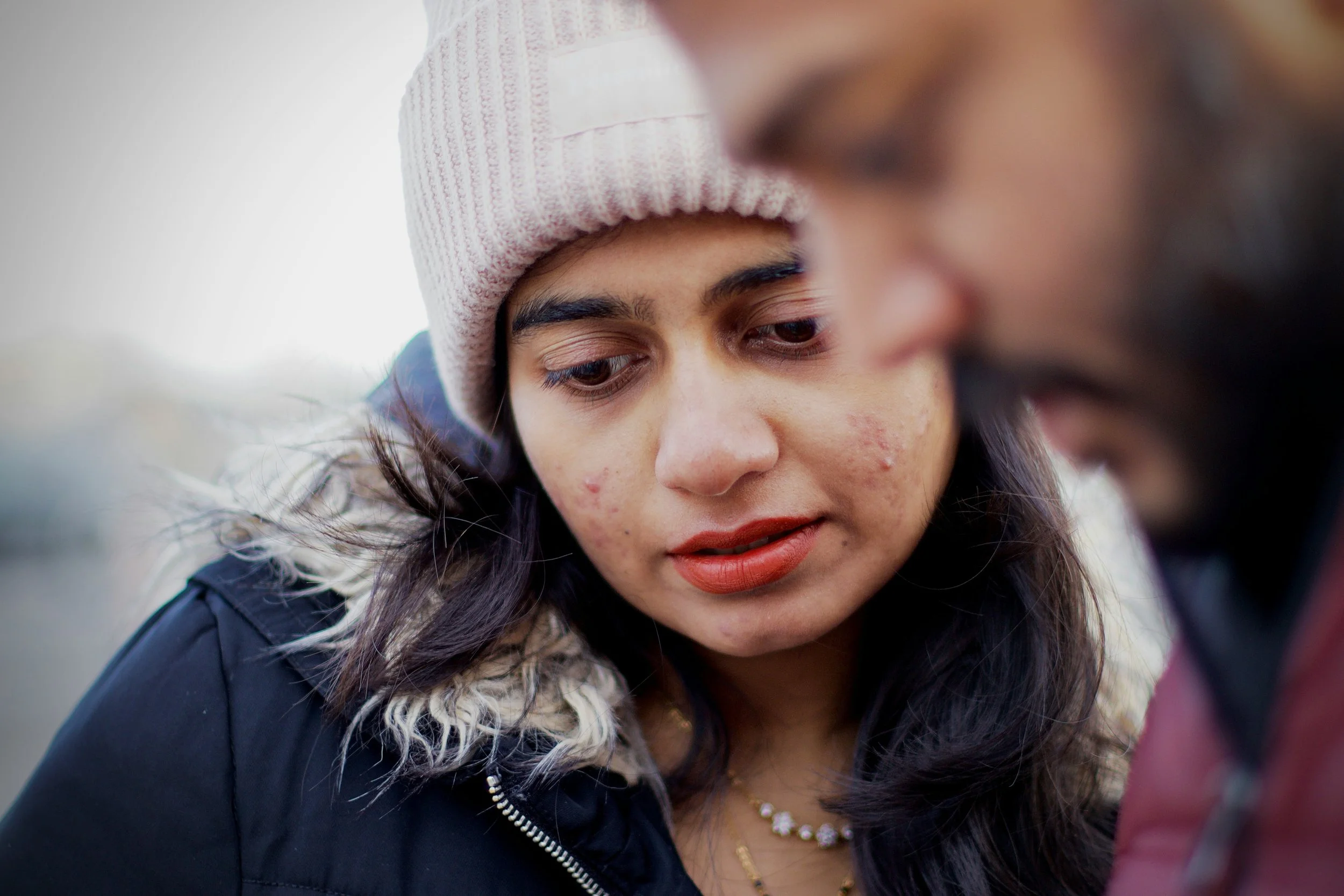 A woman wearing a coat and hat is looking at something in her male partner's hand