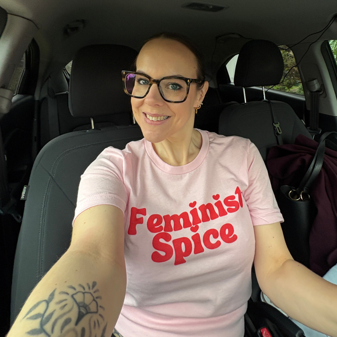 A photo of Aimee Bishop on International Women's Day 2026 wearing a baby pink t-shirt with the slogan "Feminist Spice"