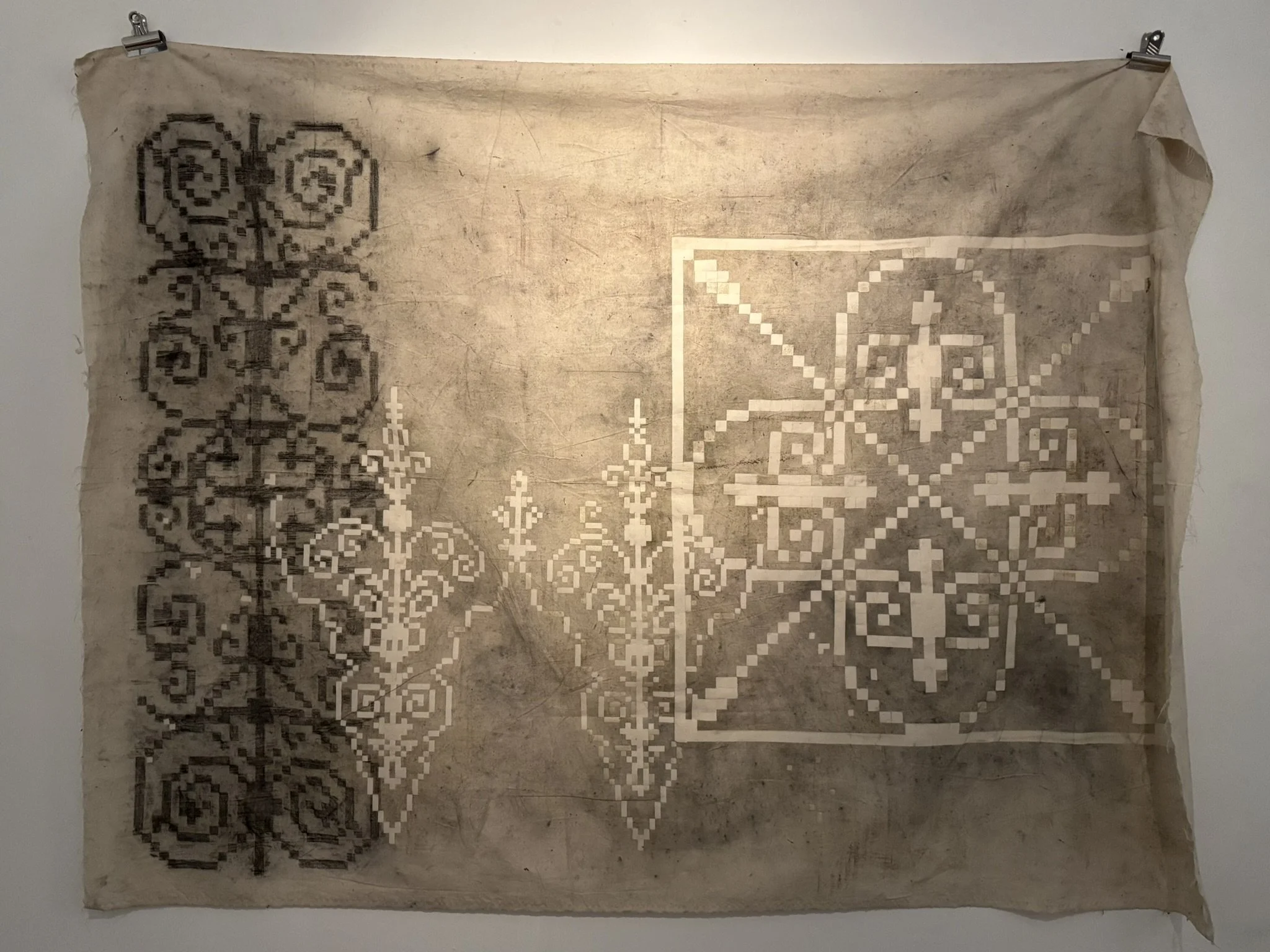 Ancient textile with geometric and floral patterns, displayed on a wall with hooks.