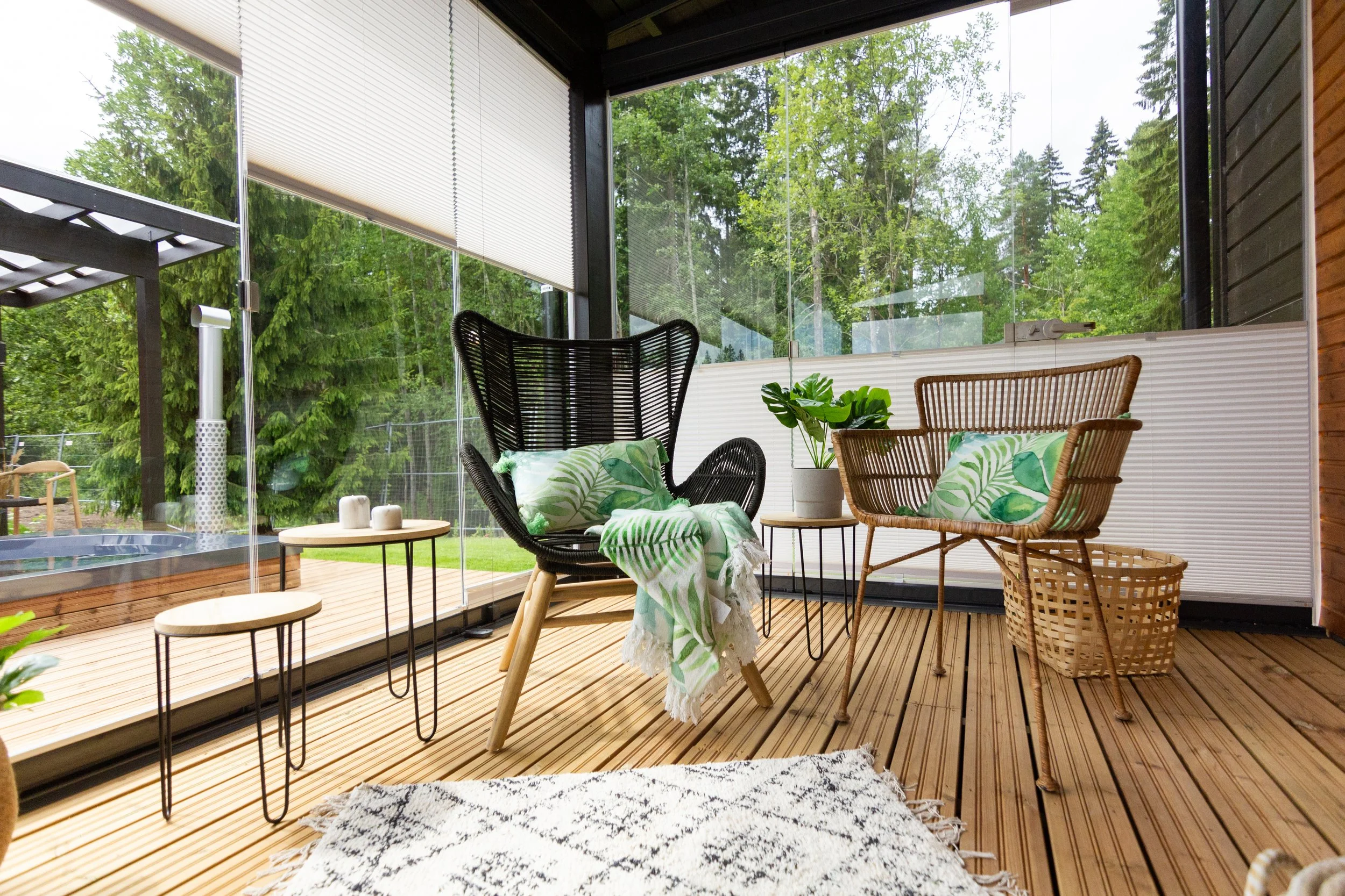 Terassi sisustettu mustalla ja luonnonvärisillä aistuilla ja vihreällä kasveilla, suuri ikkuna ympäröi tilaa ja antaa luonnon näkymän