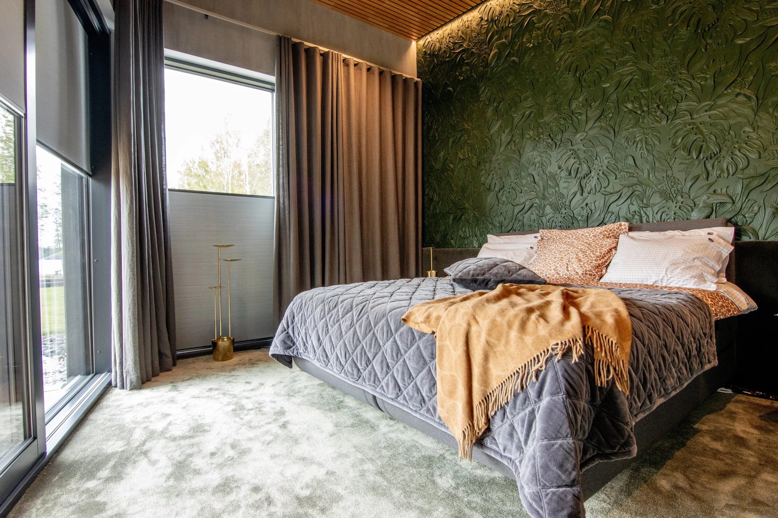 Tykki vuode, ikkunan ja verhojen äärellä, seinällä vihreä kasvokuvioinen tapetti.