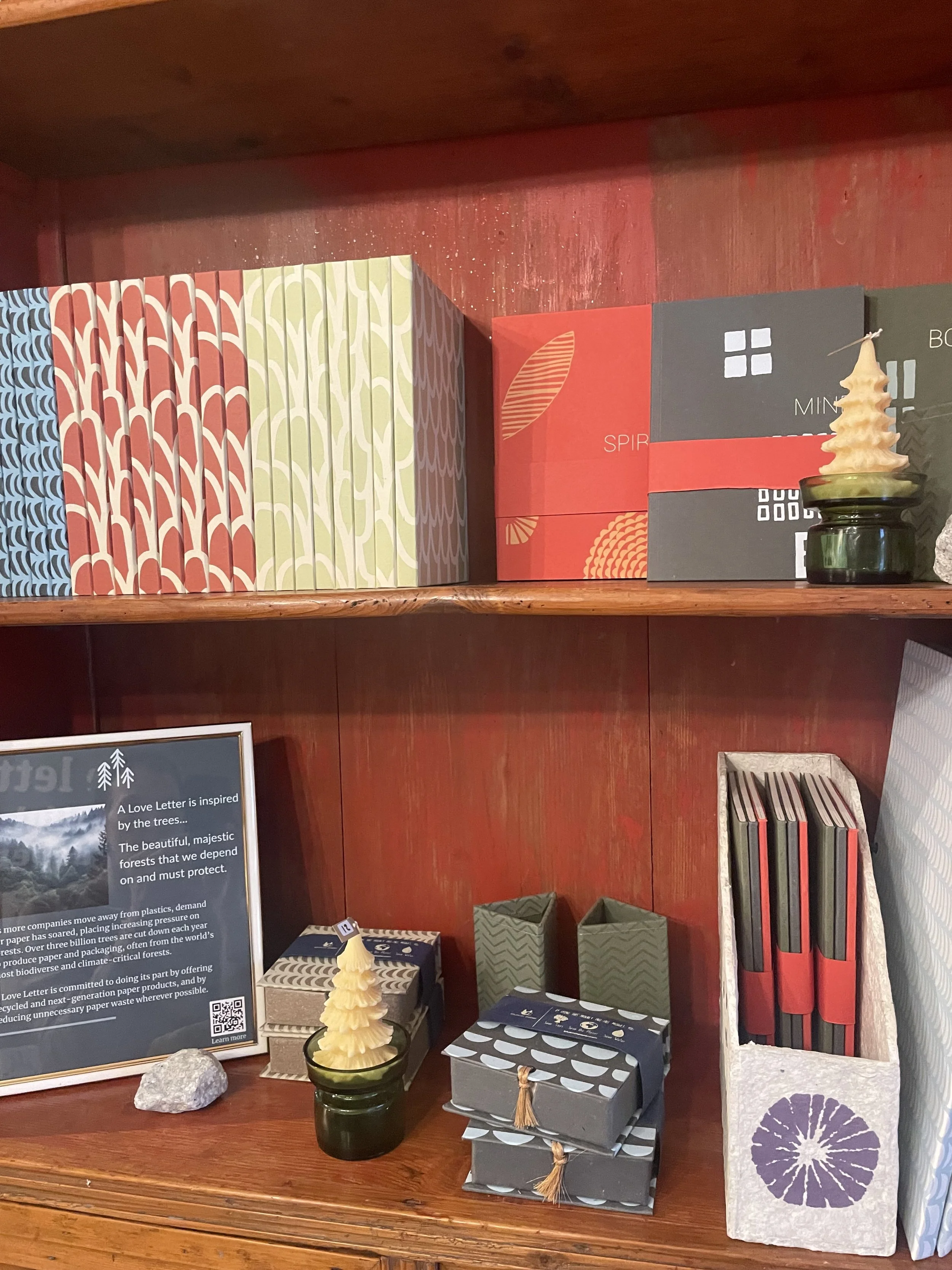 Decorative holiday display on wooden shelves featuring gift boxes, candles, and a framed sign about environmental sustainability.