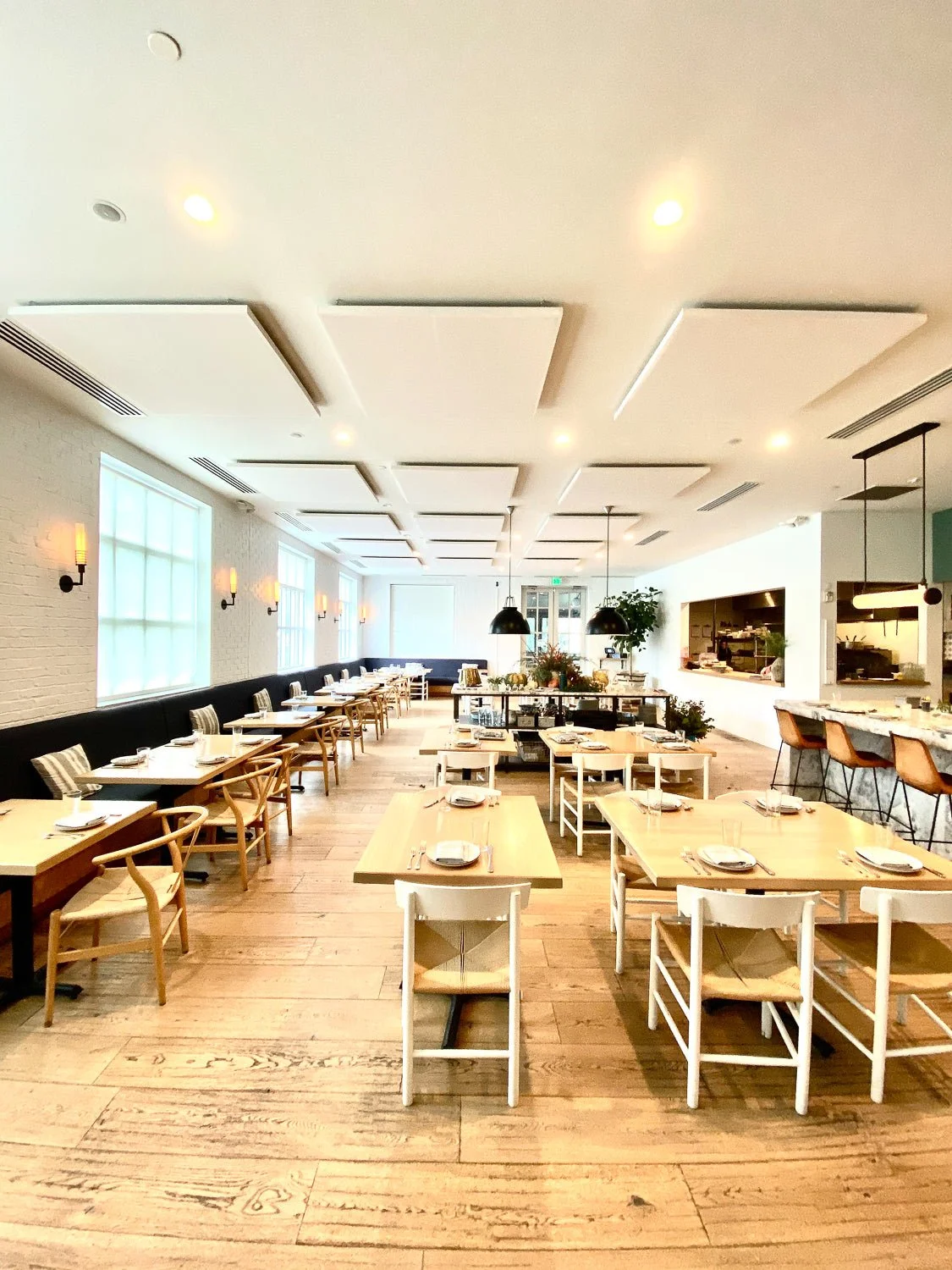 Empty restaurant dining area with wooden tables and chairs, large windows, and modern decor.