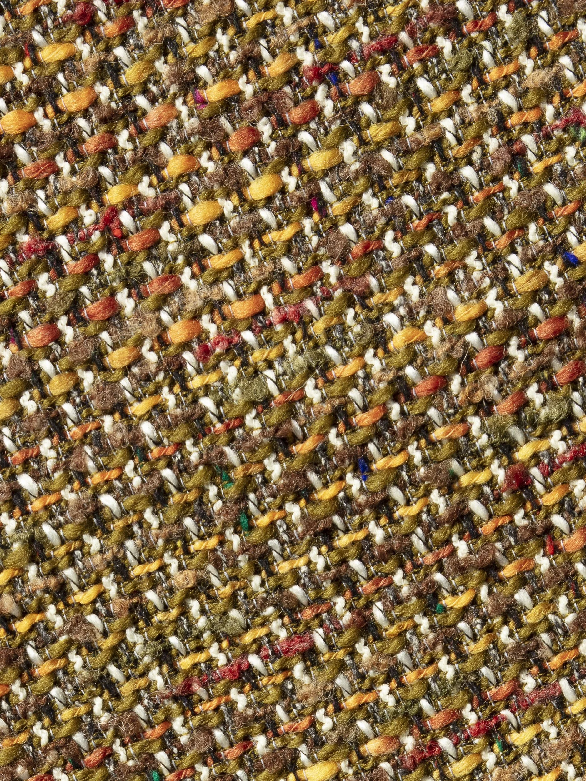 Close-up van de rijke tweedstructuur met oker, roestoranje, mosgroen en fijne kleuraccenten.
