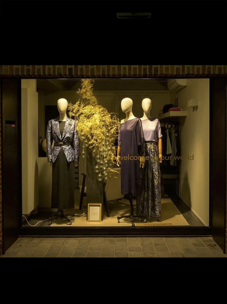 Etalage met drie mannequins gekleed in dameskleding en een grote decoratieve tak met gouden versieringen.