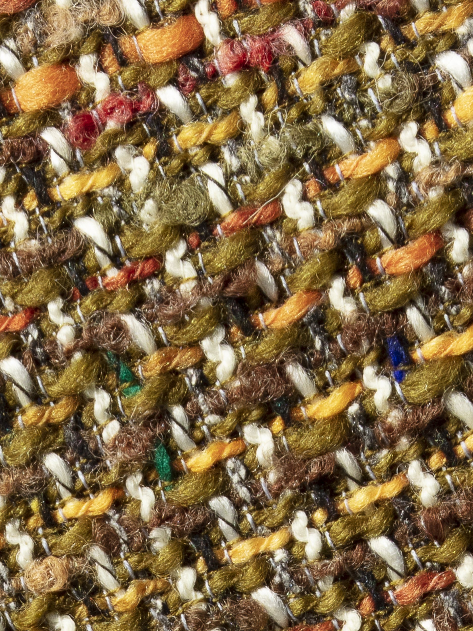 Close-up van de rijke tweedstructuur met oker, roestoranje, mosgroen en fijne kleuraccenten.