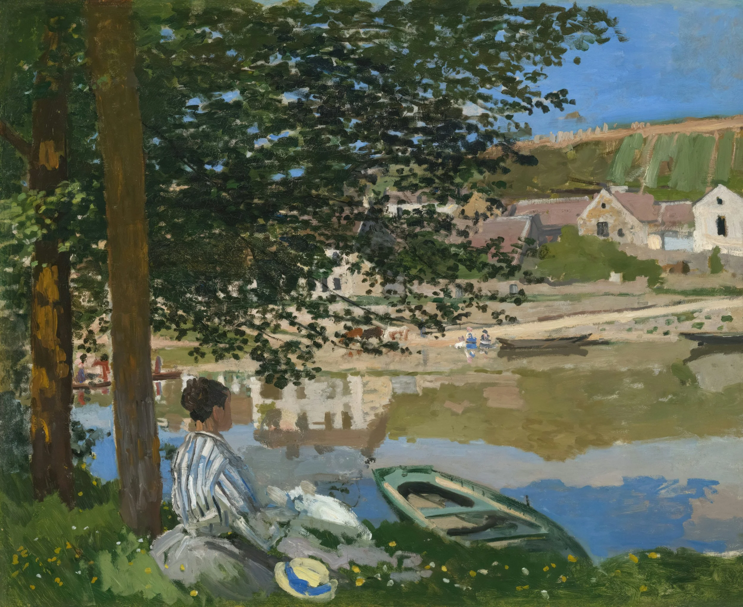 A woman sitting under trees near a river, with a hat beside her, looking at boats and houses along the riverbank on a sunny day.