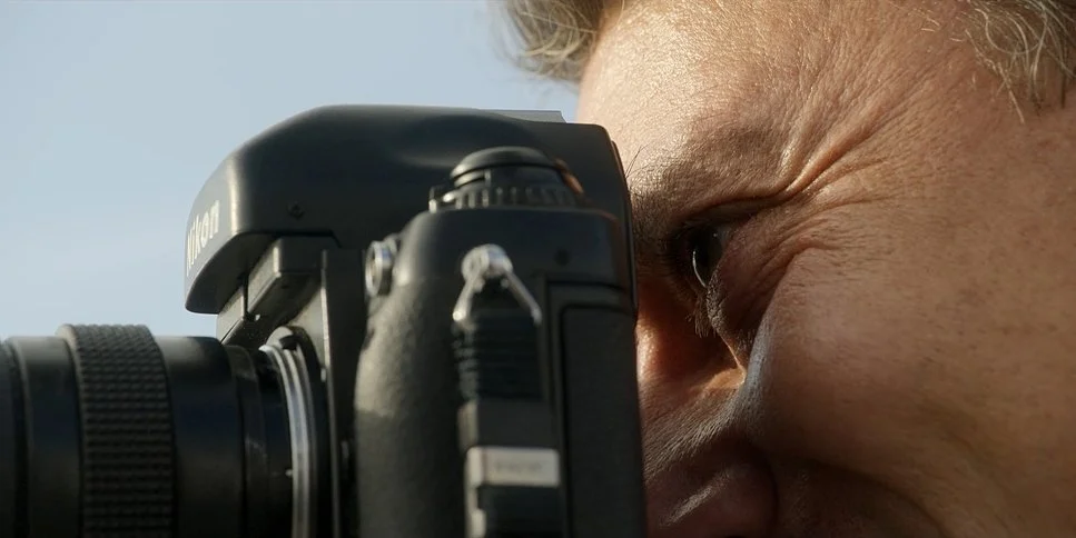 Un homme regarde à travers le viseur d'un appareil photo numérique.