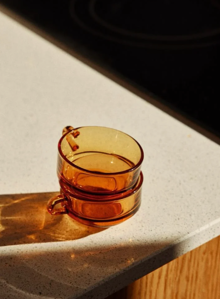 Deux petites tasses en verre orange empilées sur un plan de travail en comptoir de cuisine, avec une source lumineuse créant une ombre à gauche.