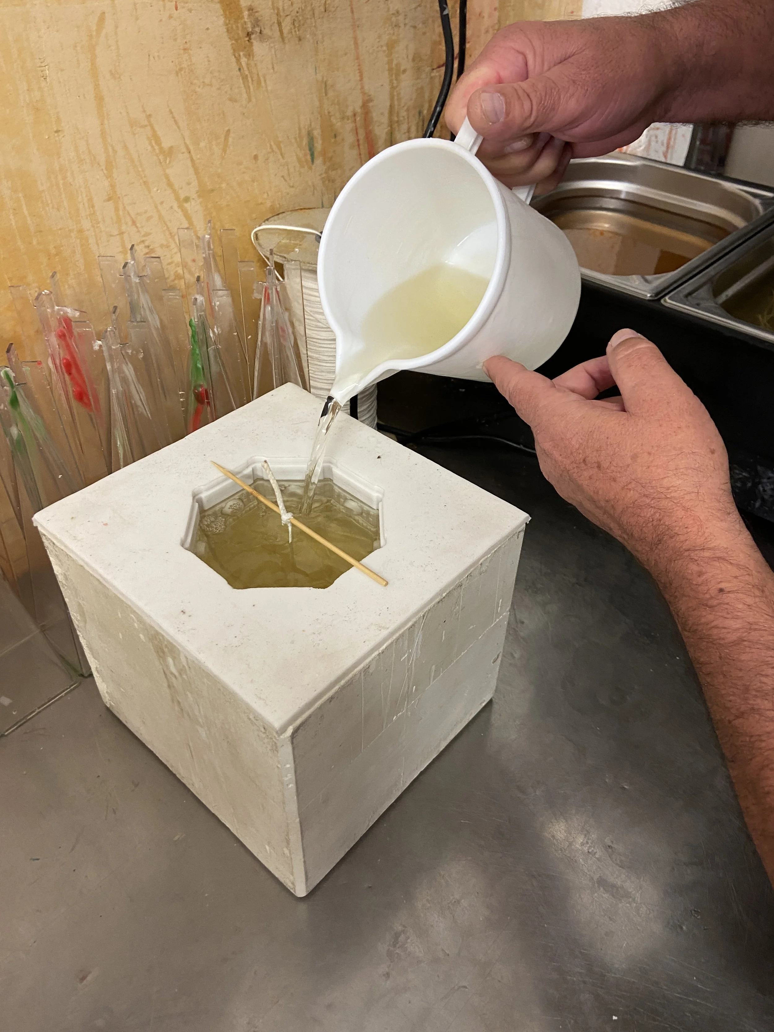Person pouring hot liquid into a melting wax mold for candle making.