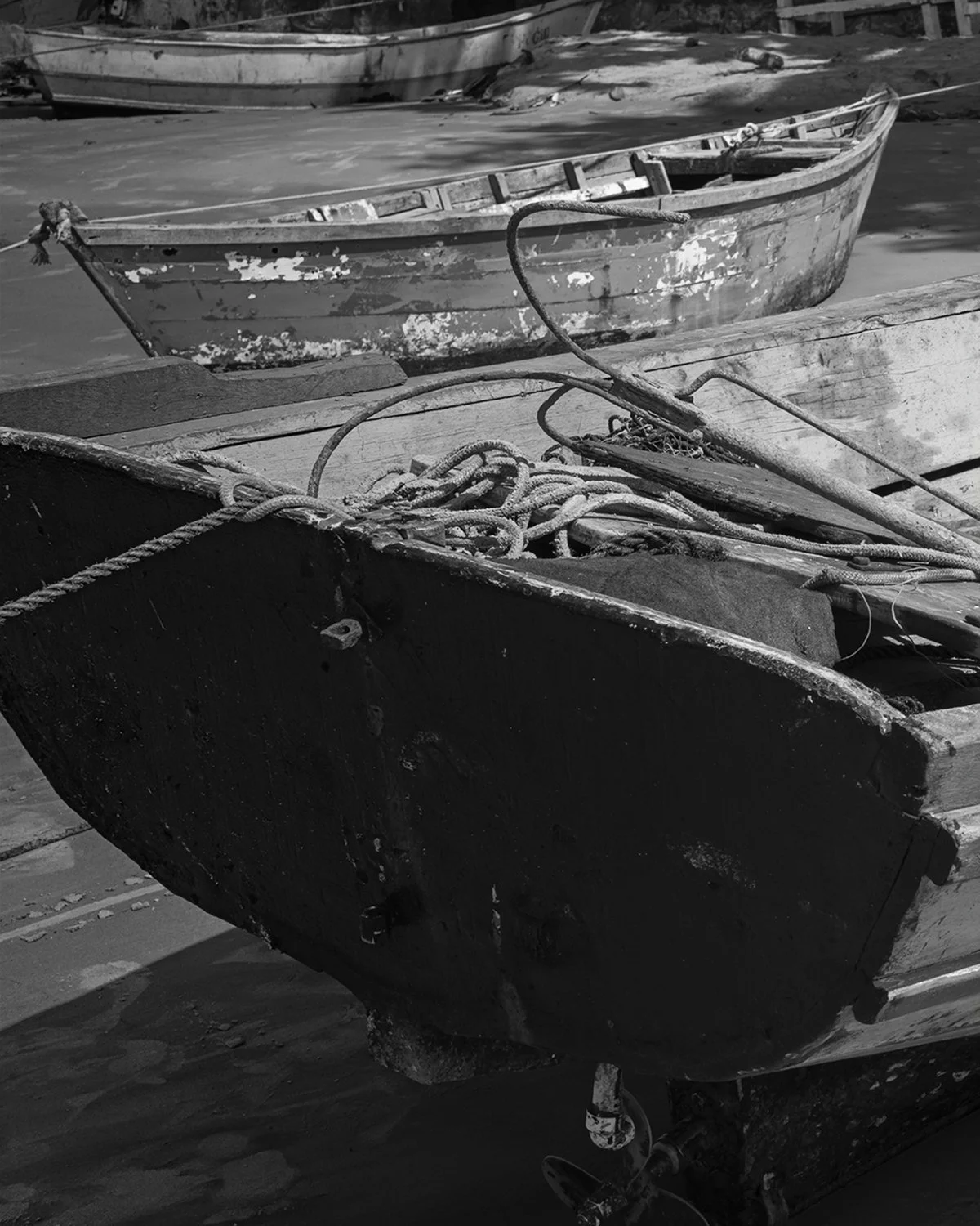 Black and white photo of old weathered boats on a dock, with ropes tied to the hulls.