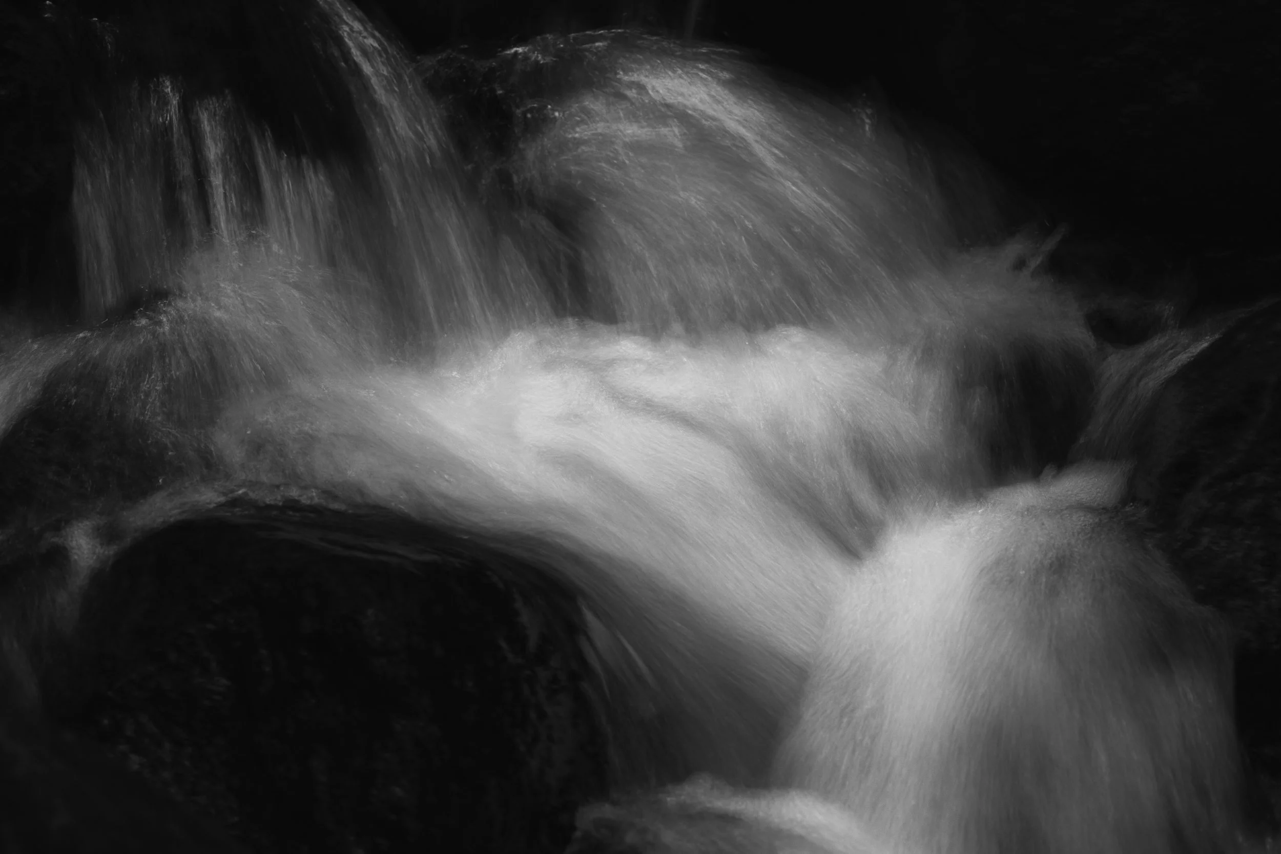 Black and white photo of rushing water in a river or stream.