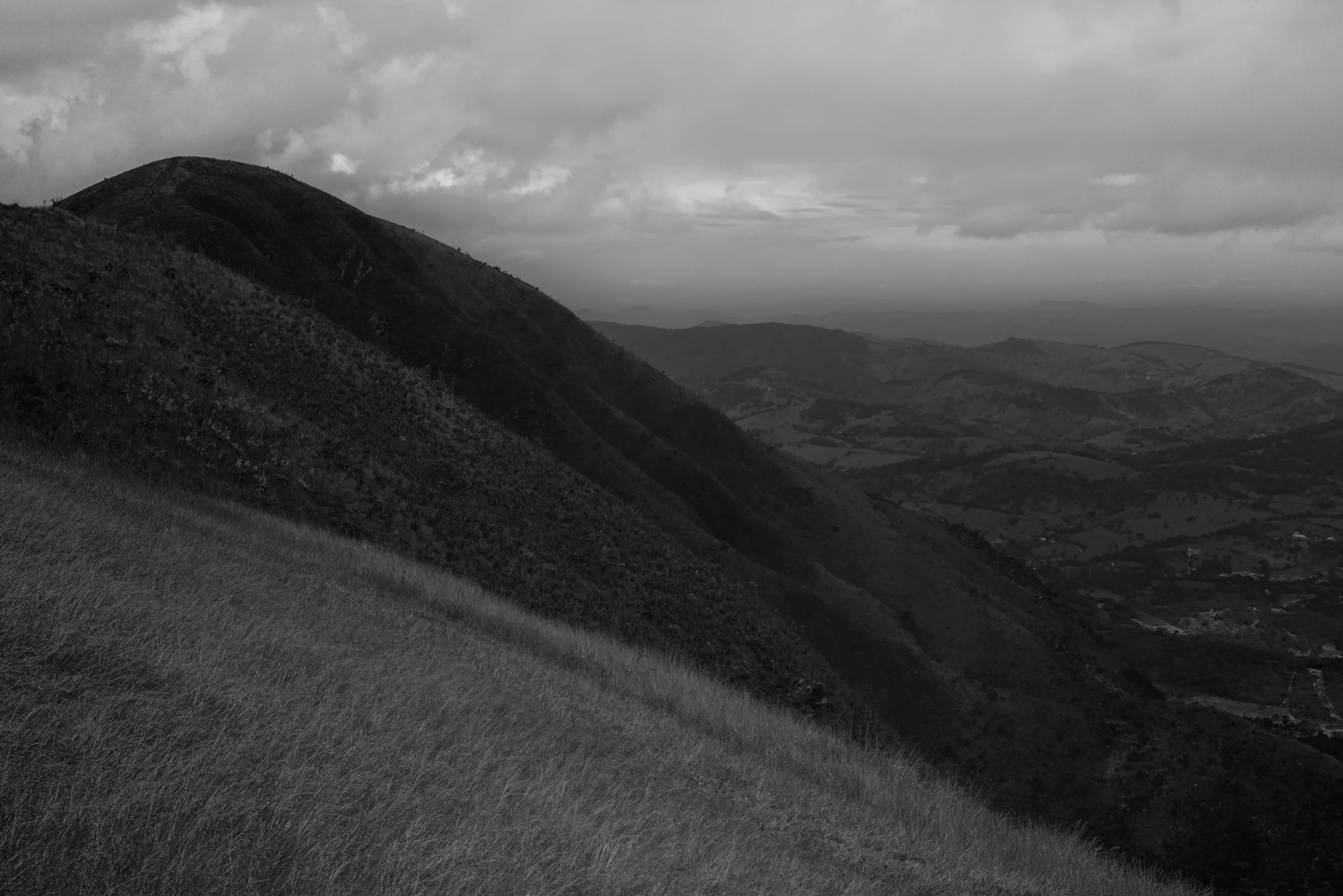 A black and white photo of a mountain landscape with rolling hills, a cloudy sky, and valleys in the distance.