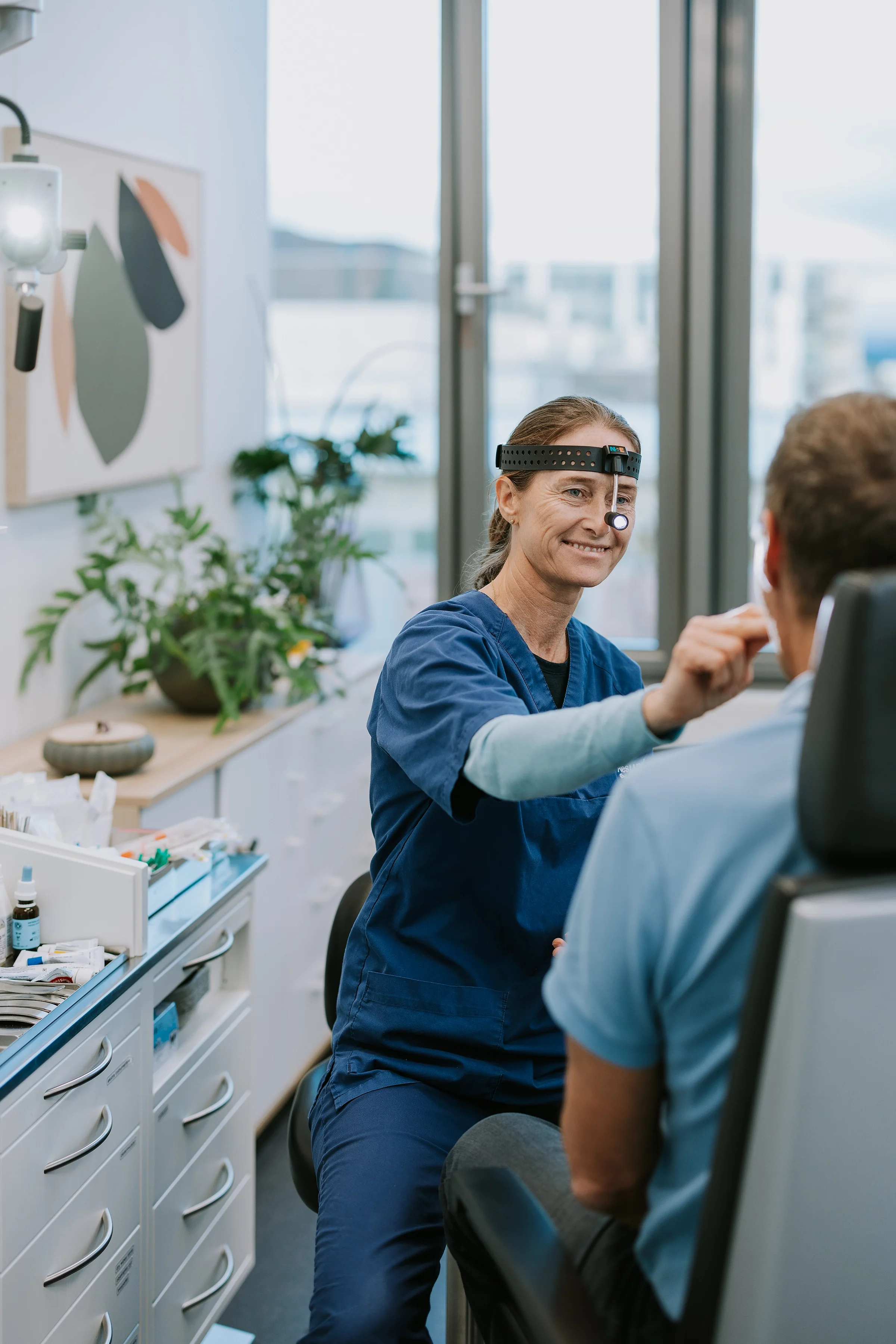 En sykepleier med medisinsk utstyr utfører en undersøkelse på en pasient i et klinikkrom.